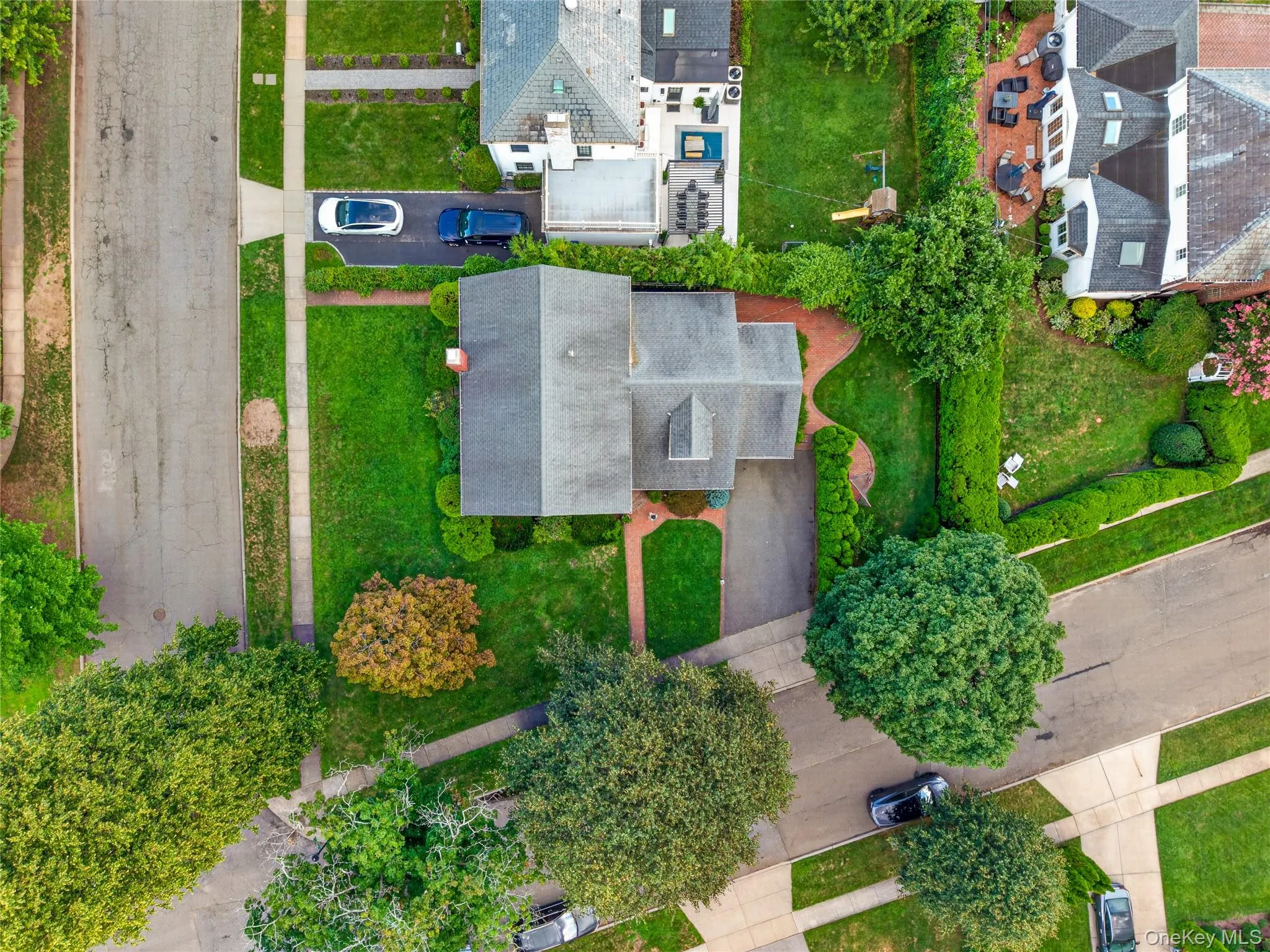 Aerial view of a residential property with a central home, an asphalt driveway, and a manicured lawn Aerial view of a residential property with a central home, an asphalt driveway, and a manicured lawn