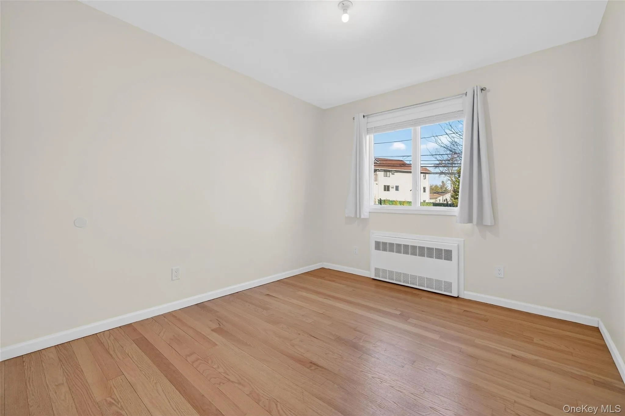 Unfurnished room with radiator heating unit and light wood finished floors Unfurnished room with radiator heating unit and light wood finished floors