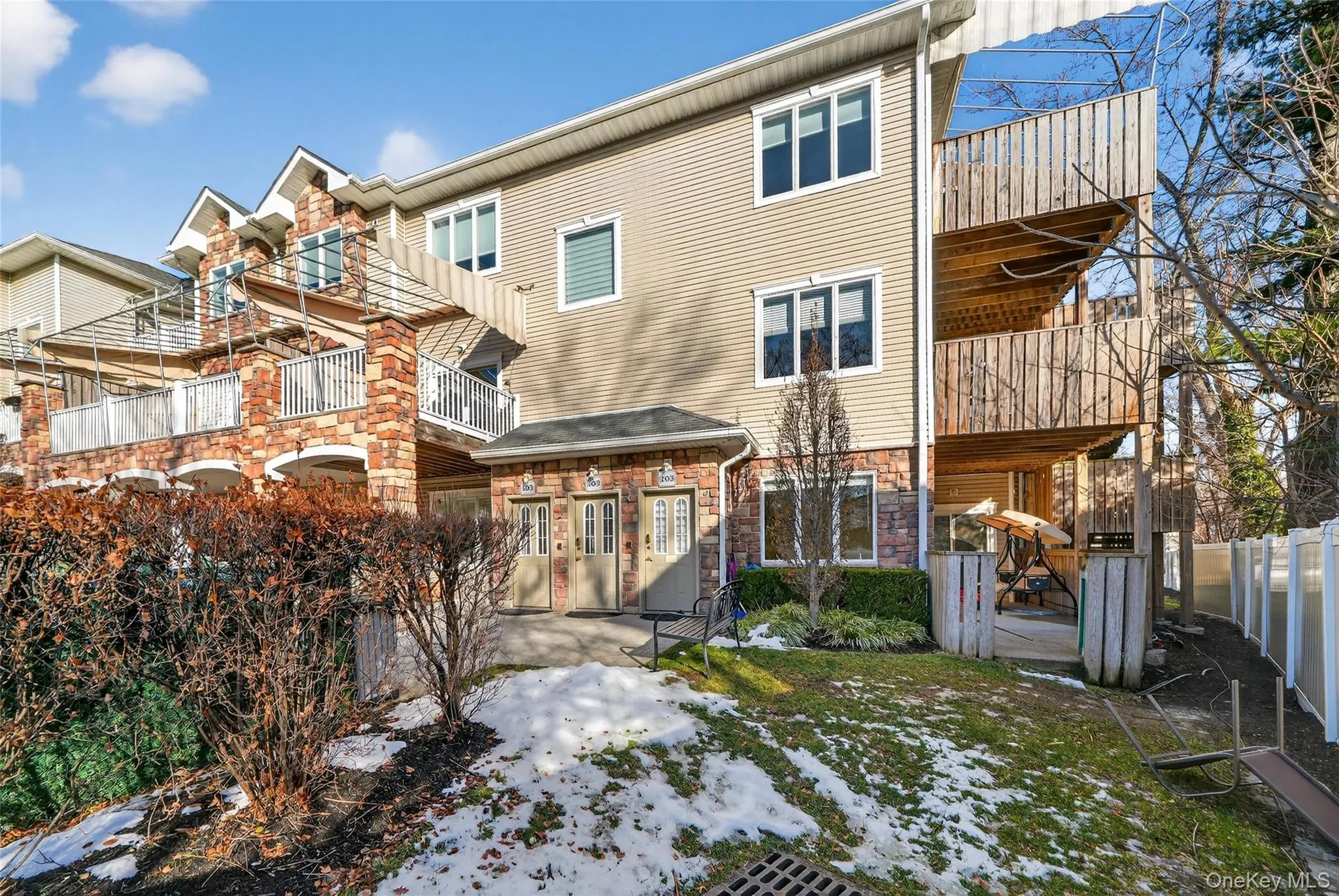 Rear view of house with a balcony, a fenced backyard, stone siding, and a patio Rear view of house with a balcony, a fenced backyard, stone siding, and a patio