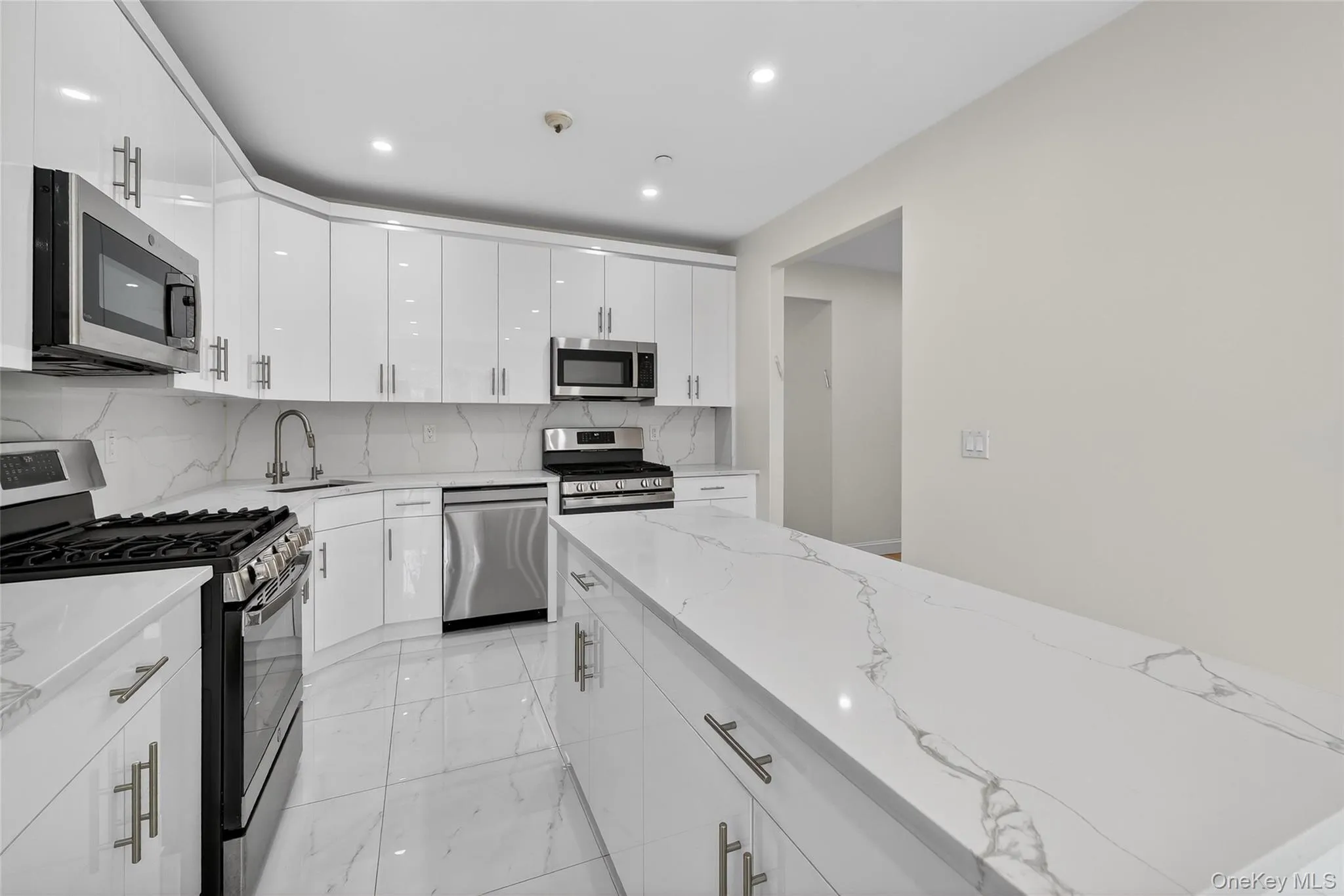 Kitchen featuring appliances with stainless steel finishes, white cabinets, light marble finish floors, modern cabinets, and light stone counters Kitchen featuring appliances with stainless steel finishes, white cabinets, light marble finish floors, modern cabinets, and light stone counters