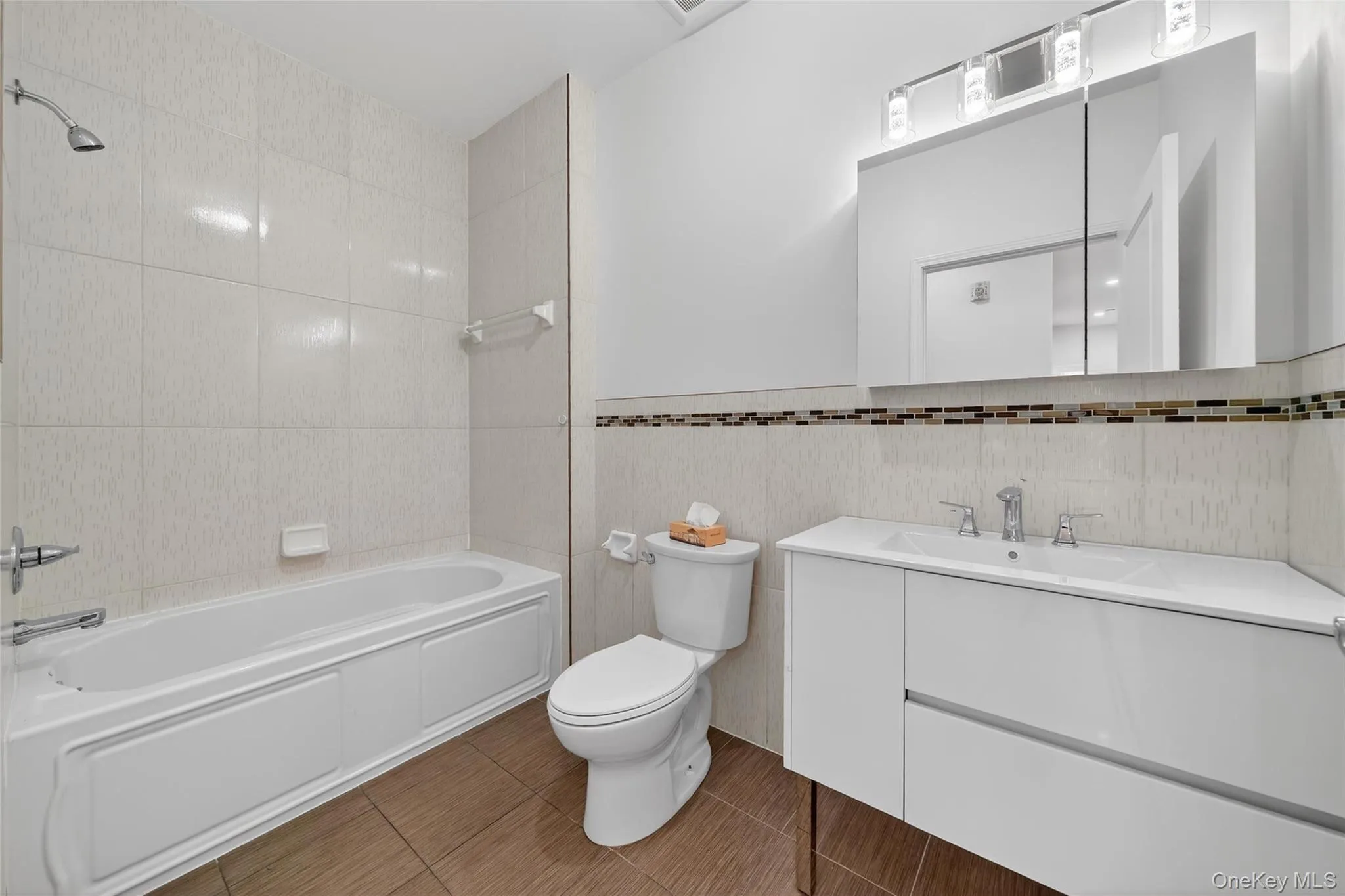 Full bath with tile walls, vanity, shower / bathtub combination, and dark tile patterned floors Full bath with tile walls, vanity, shower / bathtub combination, and dark tile patterned floors