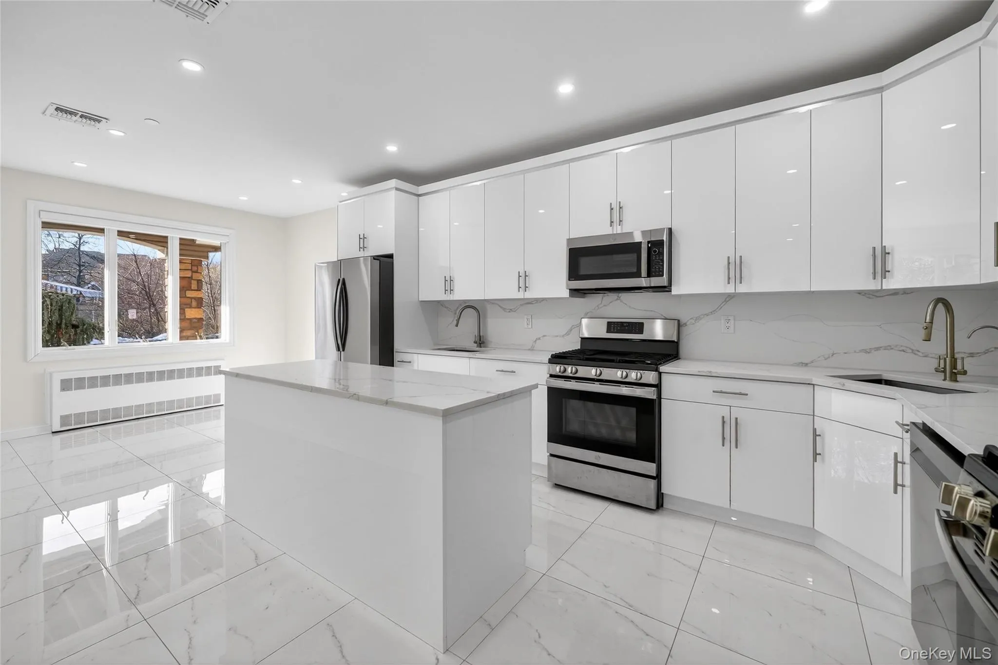 Kitchen with stainless steel appliances, a center island, white cabinetry, radiator heating unit, and light stone countertops Kitchen with stainless steel appliances, a center island, white cabinetry, radiator heating unit, and light stone countertops