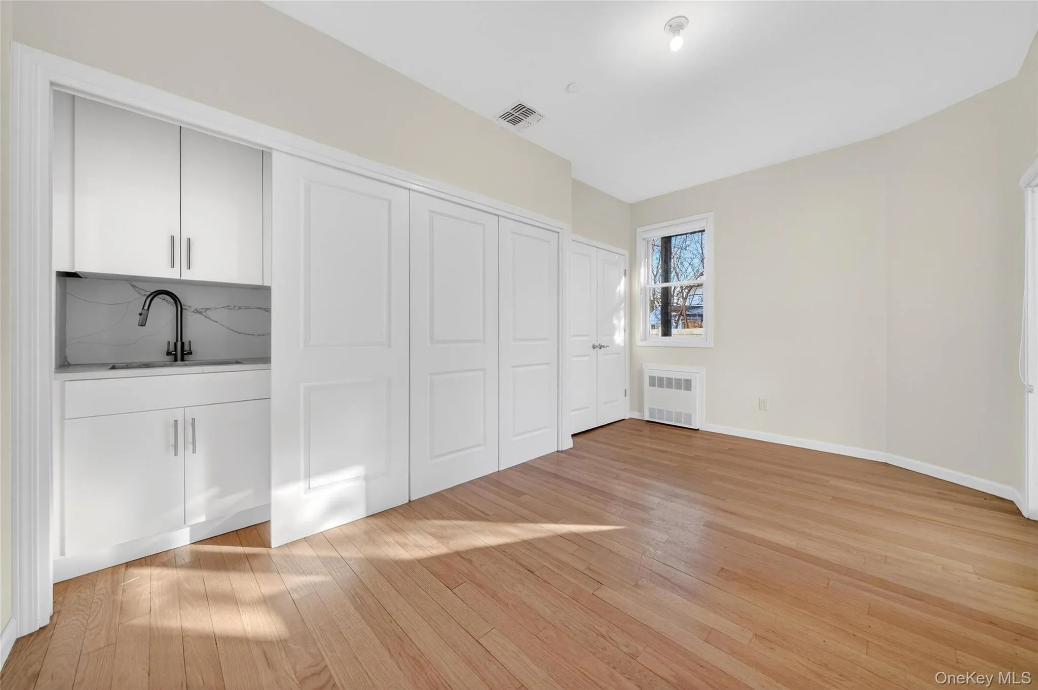 Unfurnished bedroom with light wood finished floors, a closet, and radiator Unfurnished bedroom with light wood finished floors, a closet, and radiator