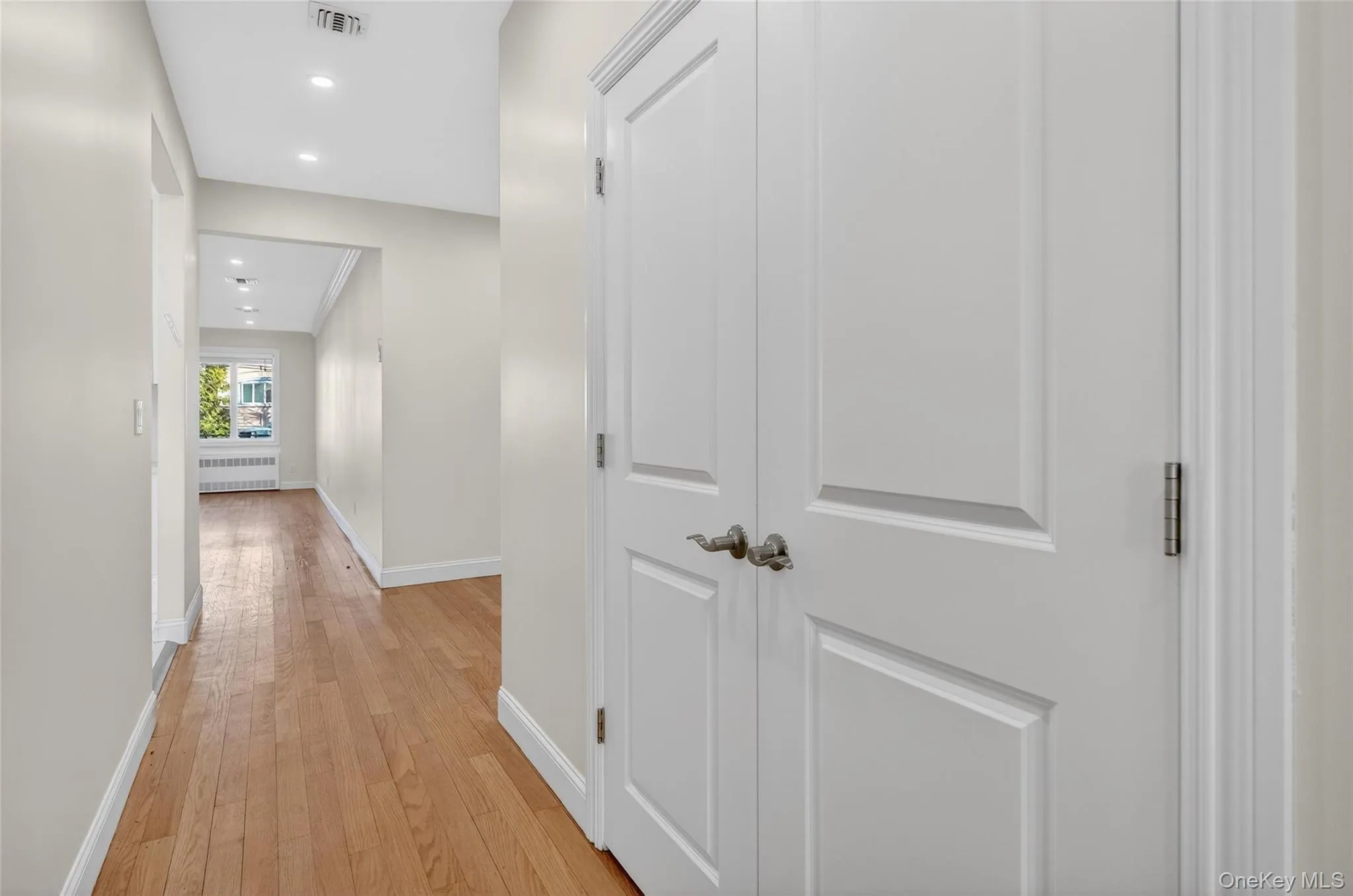 Hallway featuring light wood-type flooring, recessed lighting, and radiator Hallway featuring light wood-type flooring, recessed lighting, and radiator