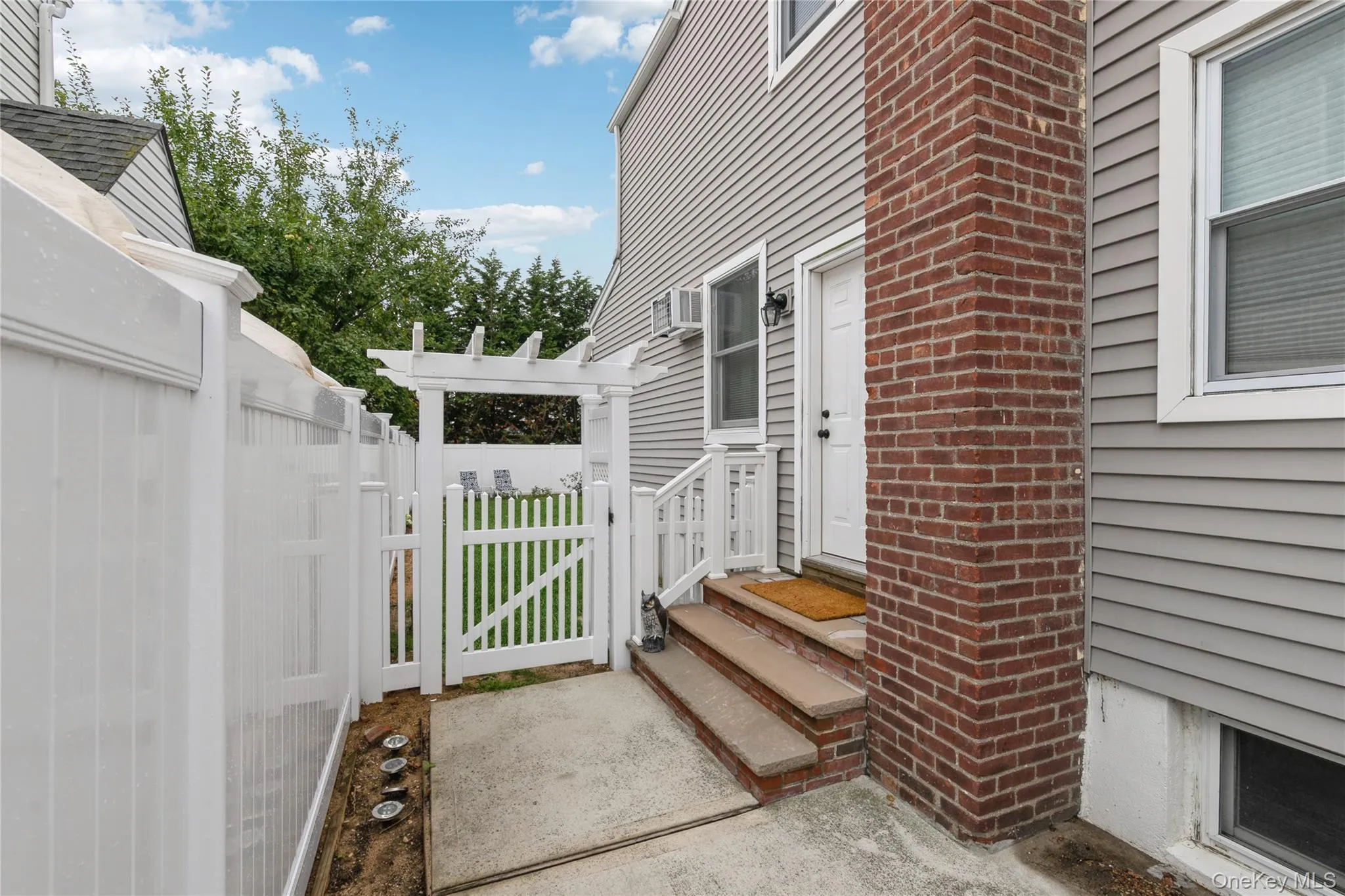 Private side entrance with a gated walkway, brick steps, and white vinyl fencing, offering convenient access and added privacy. Private side entrance with a gated walkway, brick steps, and white vinyl fencing, offering convenient access and added privacy.