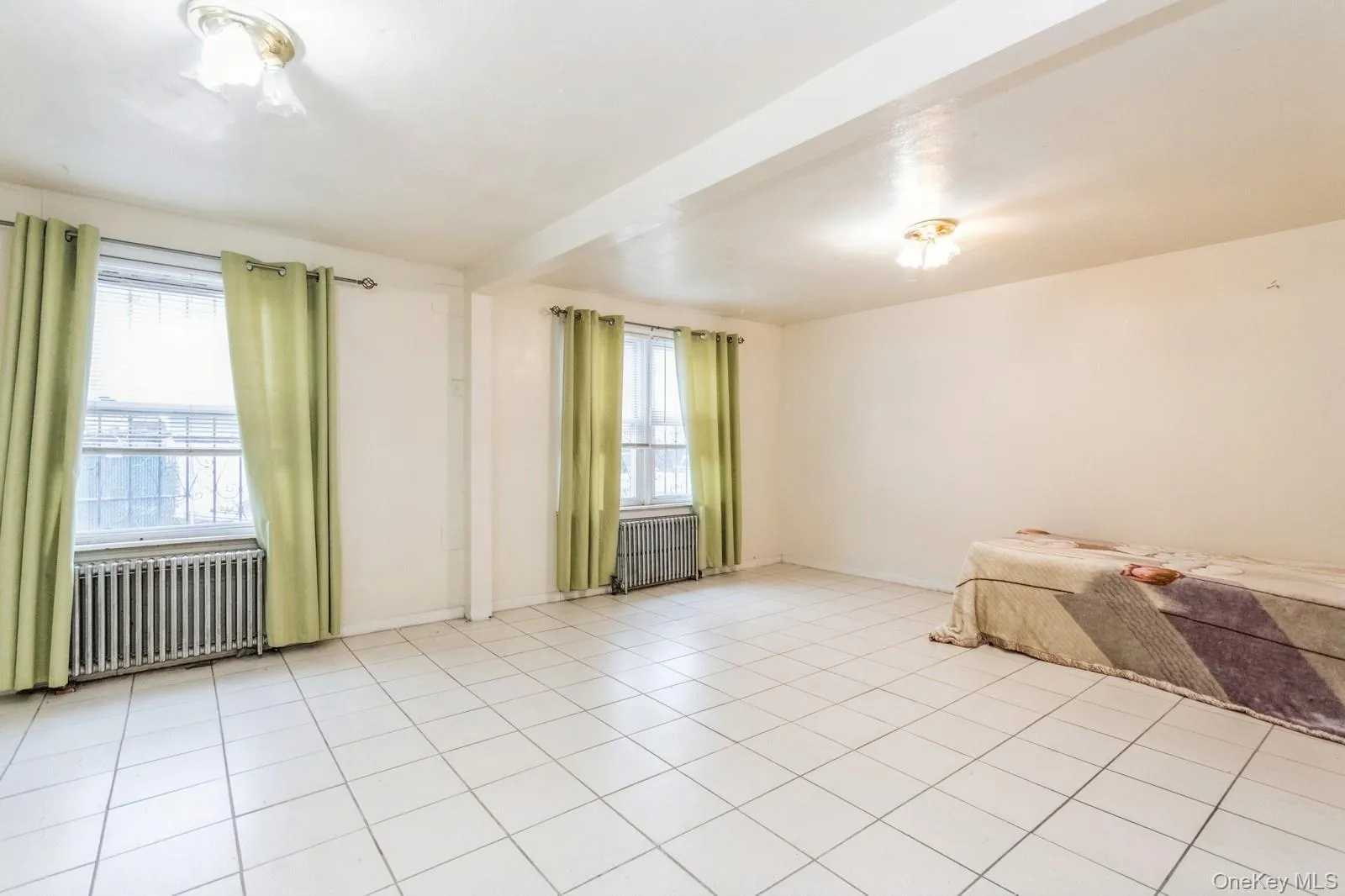 Unfurnished living room with radiator heating unit, light tile patterned floors. Unfurnished living room with radiator heating unit, light tile patterned floors.
