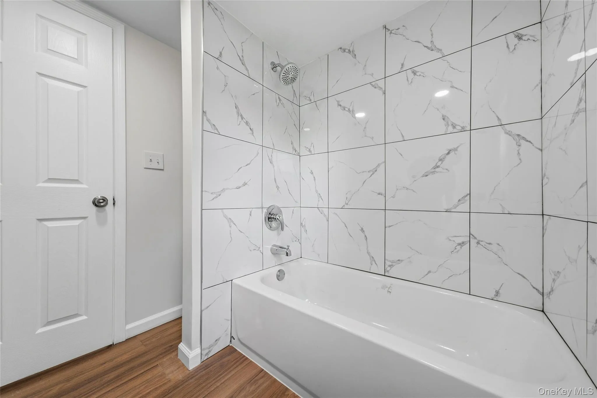 Bathtub with white subway tile surround featuring gray veining and chrome fixtures Bathtub with white subway tile surround featuring gray veining and chrome fixtures