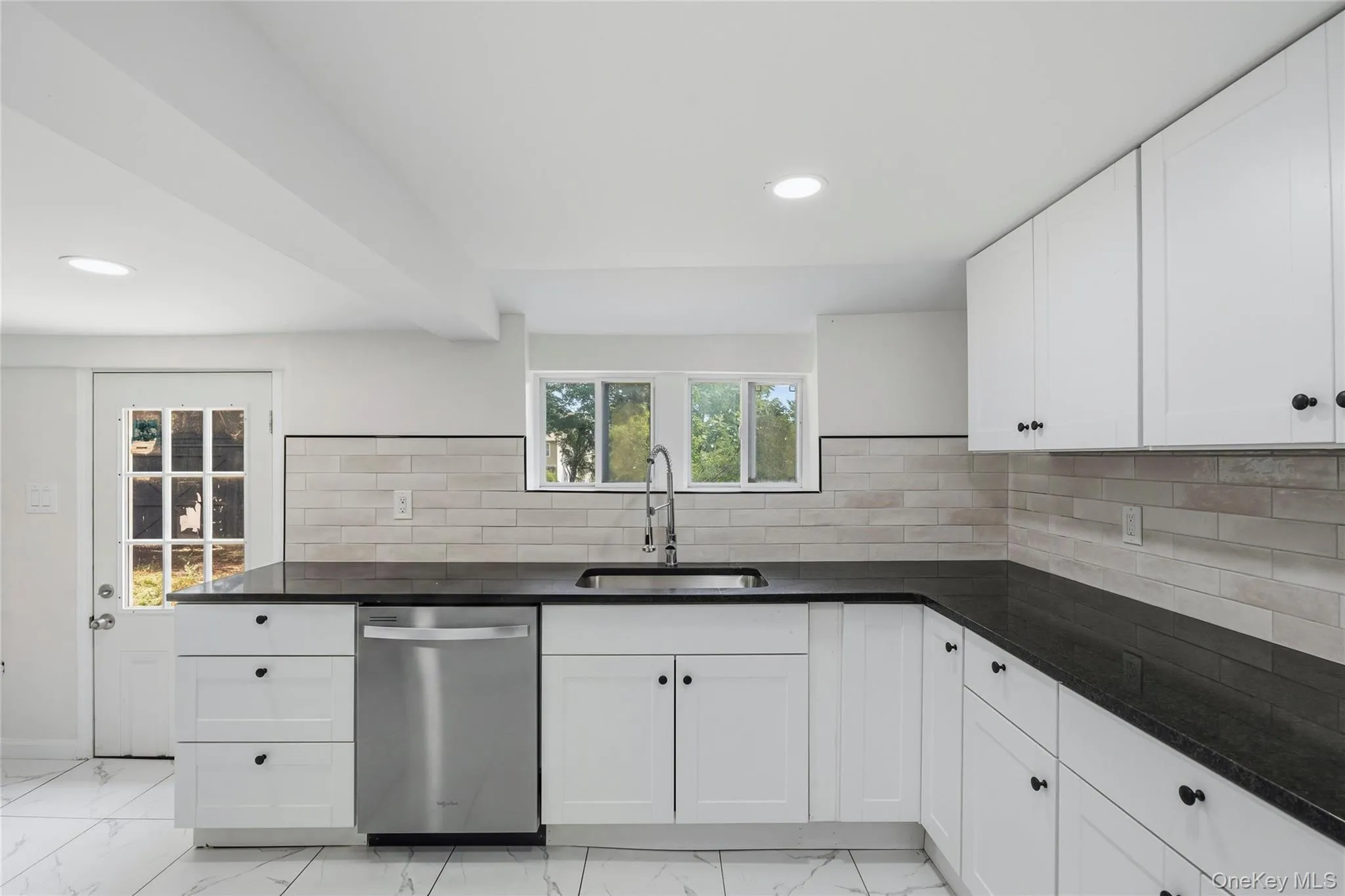 Kitchen featuring white shaker-style cabinetry, black countertops, and a stainless steel dishwasher Kitchen featuring white shaker-style cabinetry, black countertops, and a stainless steel dishwasher