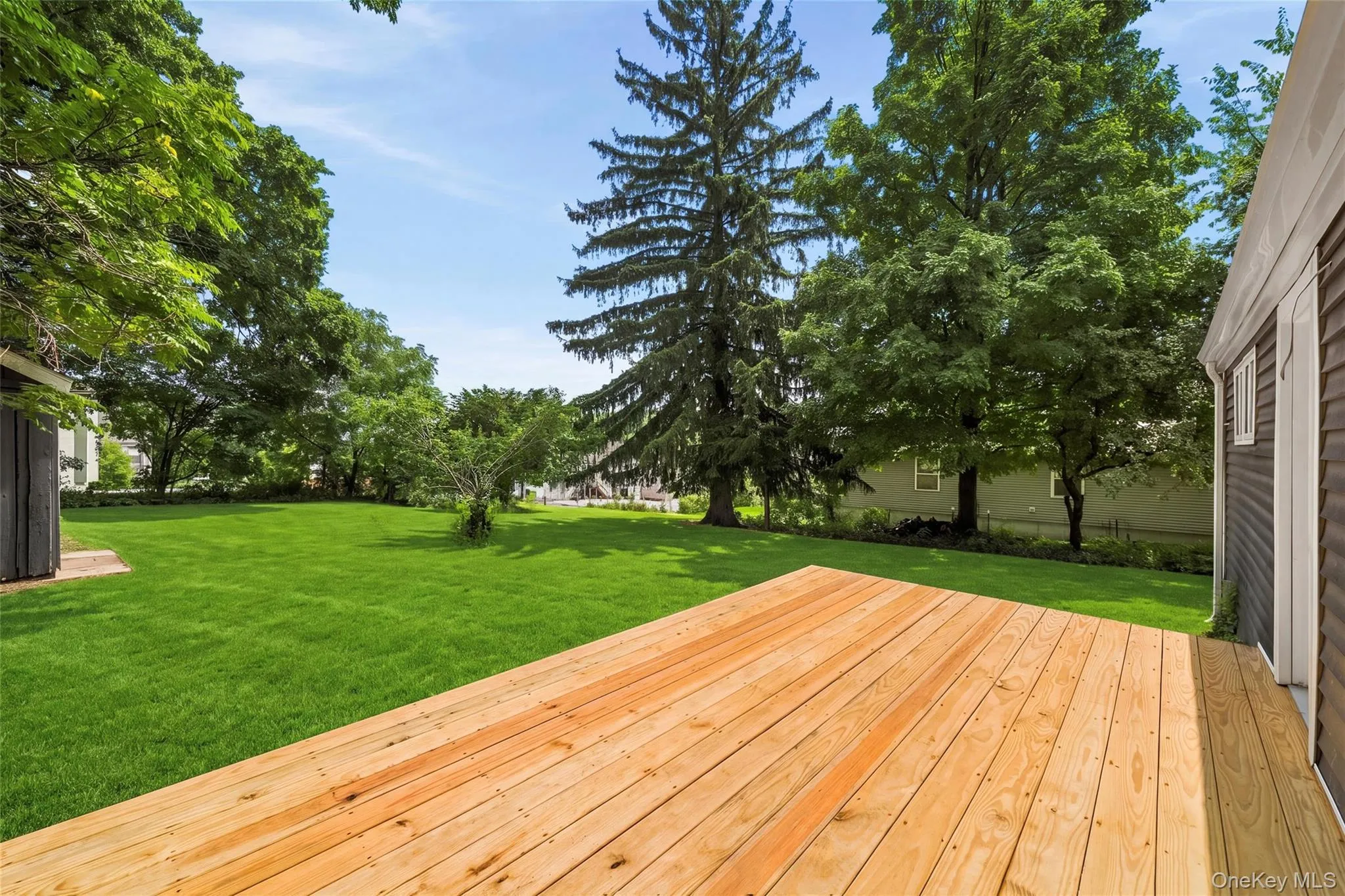 Expansive backyard featuring a new wood deck, a manicured lawn, and mature trees providing natural screening Expansive backyard featuring a new wood deck, a manicured lawn, and mature trees providing natural screening