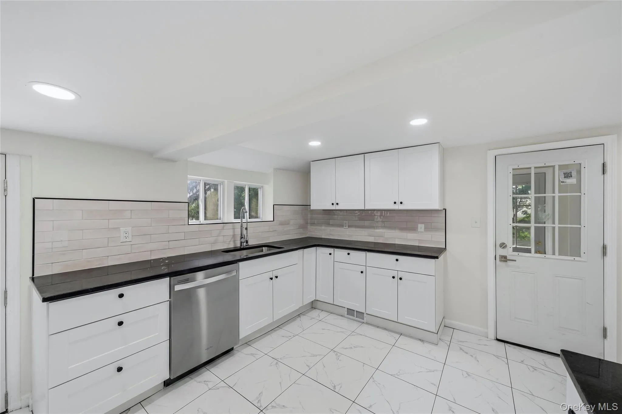Modern kitchen featuring white cabinetry, dark countertops, a stainless steel dishwasher, a window over the sink, and recessed lighting Modern kitchen featuring white cabinetry, dark countertops, a stainless steel dishwasher, a window over the sink, and recessed lighting