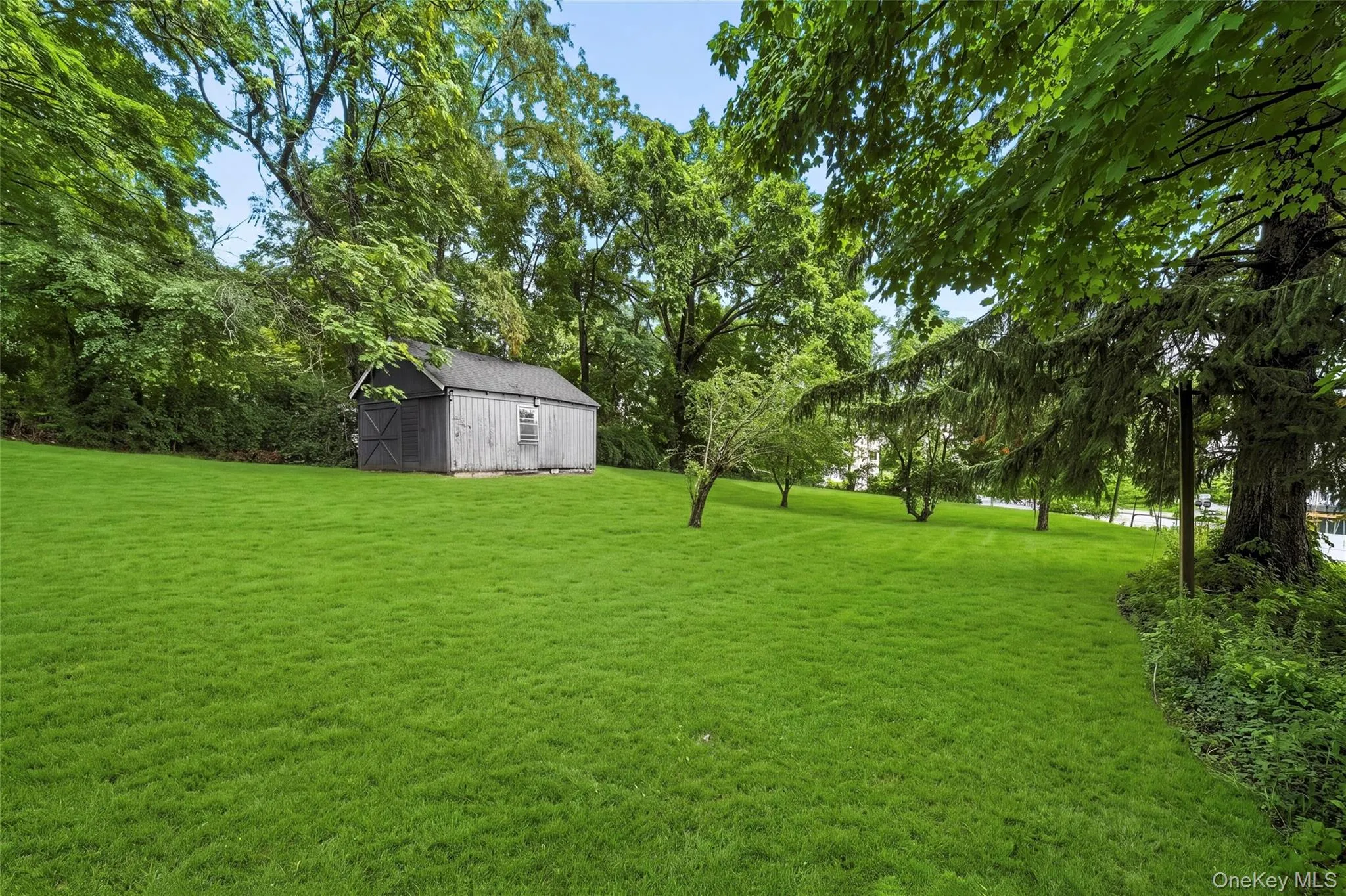 Expansive green lawn featuring a gray wood-sided storage shed with a dark roof, surrounded by mature trees Expansive green lawn featuring a gray wood-sided storage shed with a dark roof, surrounded by mature trees