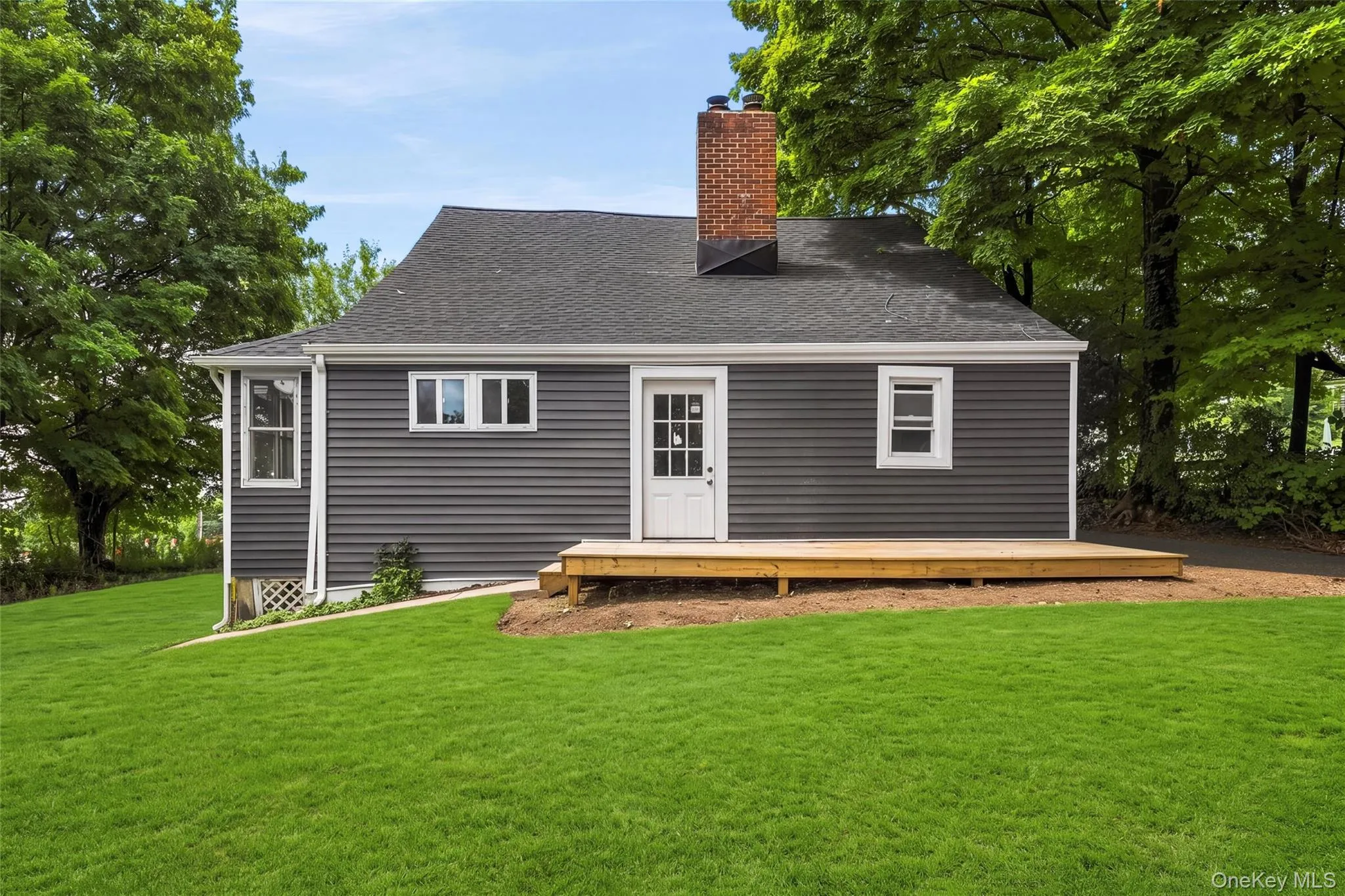 Exterior featuring dark gray siding, a newly constructed wooden deck, a brick chimney, and a black shingle roof Exterior featuring dark gray siding, a newly constructed wooden deck, a brick chimney, and a black shingle roof