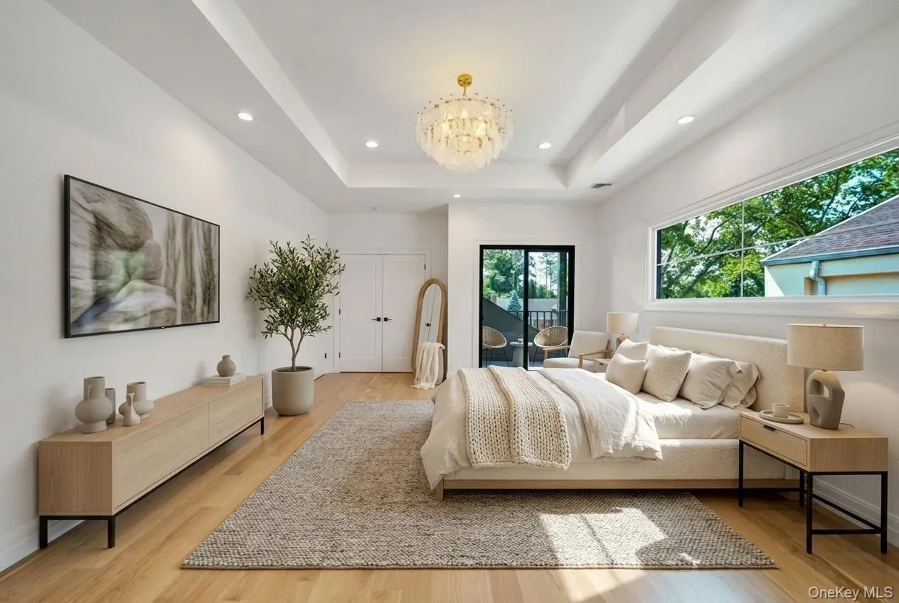Spacious room featuring light wood-finish flooring, a tray ceiling with recessed lighting, and a prominent decorative chandelier Spacious room featuring light wood-finish flooring, a tray ceiling with recessed lighting, and a prominent decorative chandelier