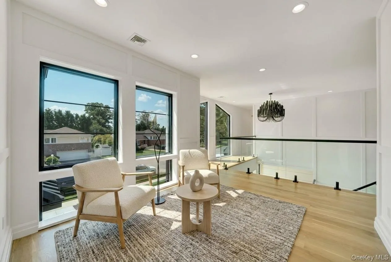 Bright open-concept space featuring large black-framed windows, light wood-finish flooring, and a glass-paneled railing with black accents Bright open-concept space featuring large black-framed windows, light wood-finish flooring, and a glass-paneled railing with black accents