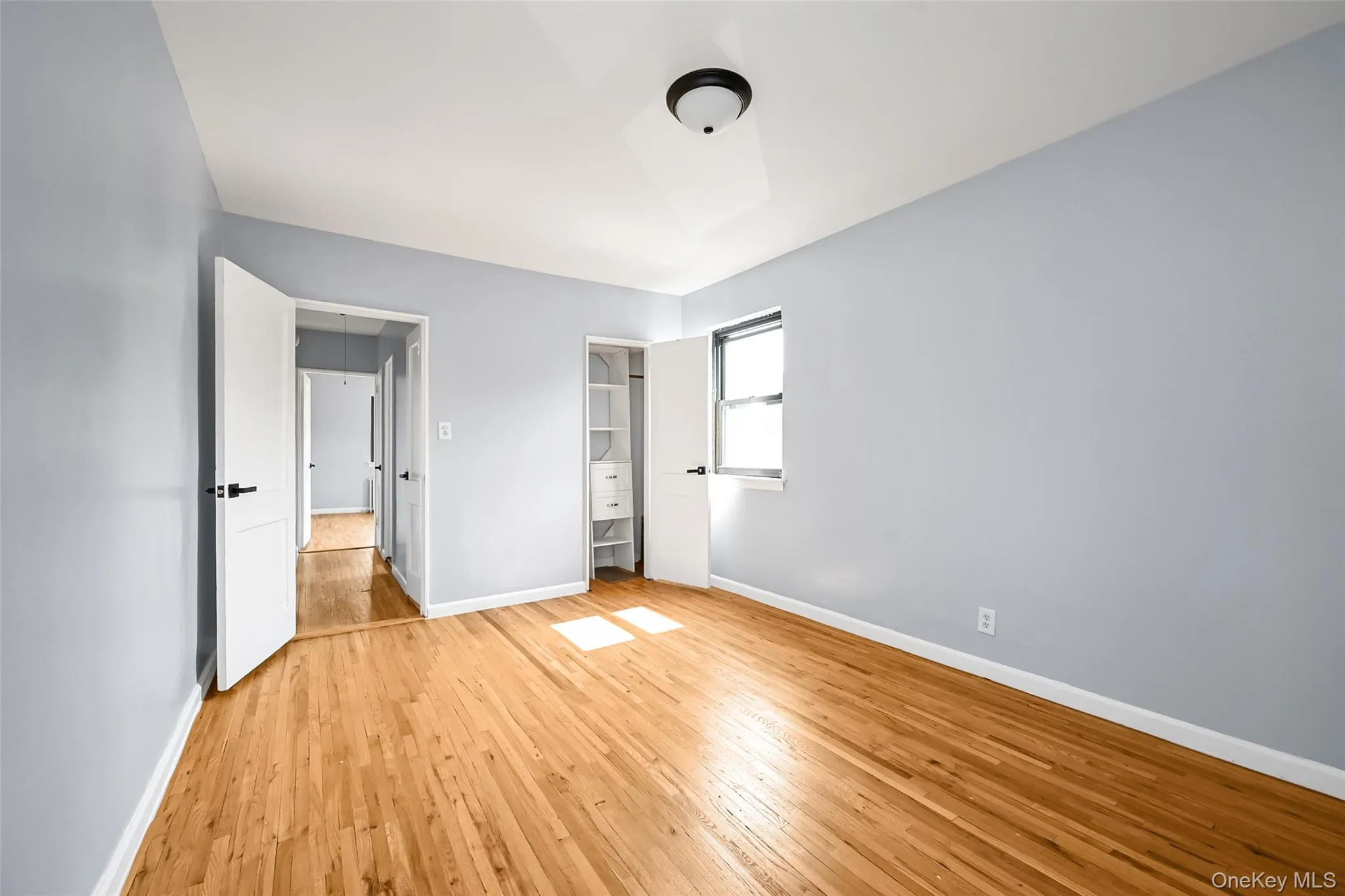 Bright room featuring wood-finish flooring, light blue walls, and a ceiling-mounted light fixture Bright room featuring wood-finish flooring, light blue walls, and a ceiling-mounted light fixture