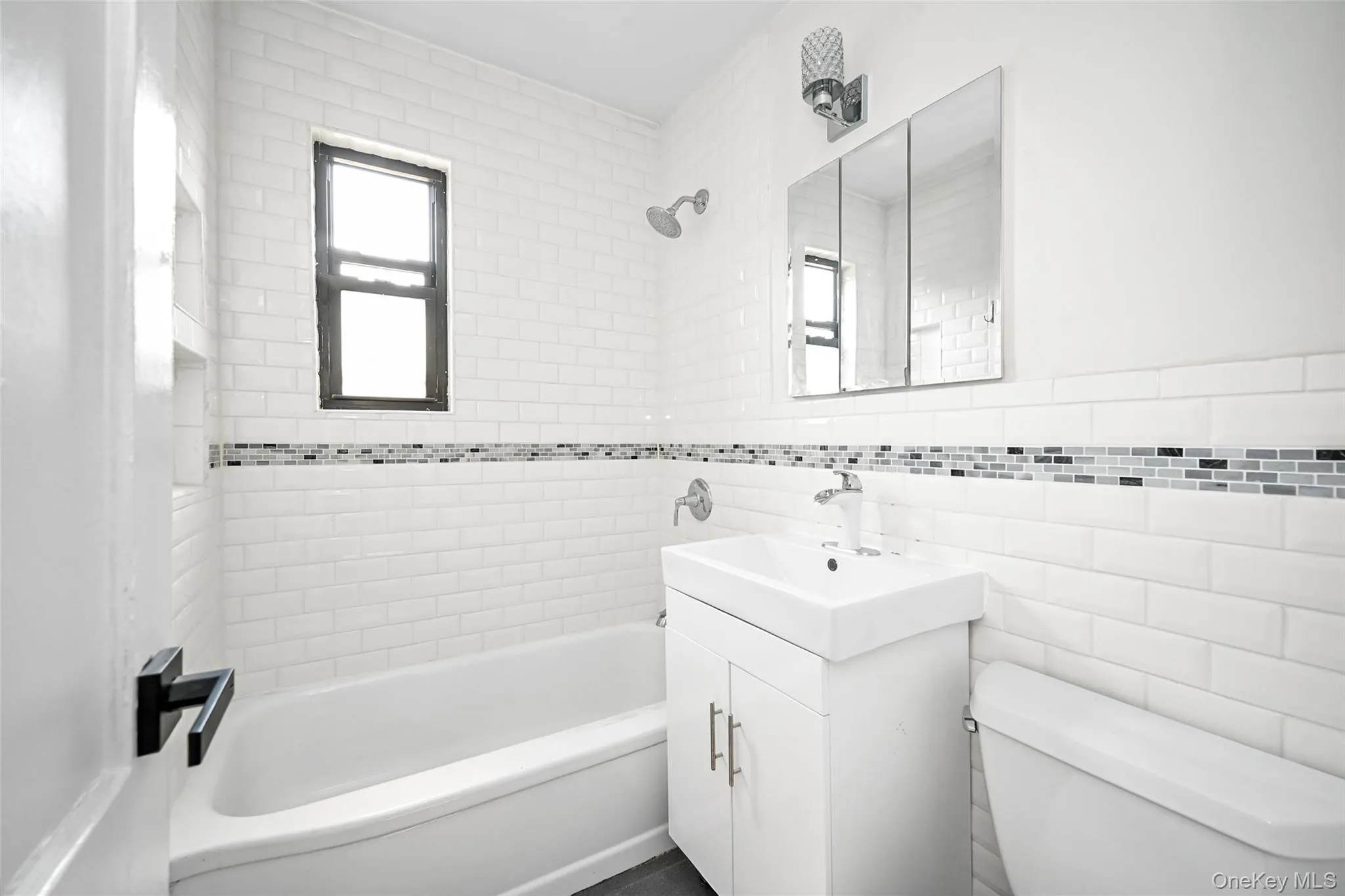 Bathroom featuring a white subway tile surround with a mosaic accent band, bathtub, and window Bathroom featuring a white subway tile surround with a mosaic accent band, bathtub, and window