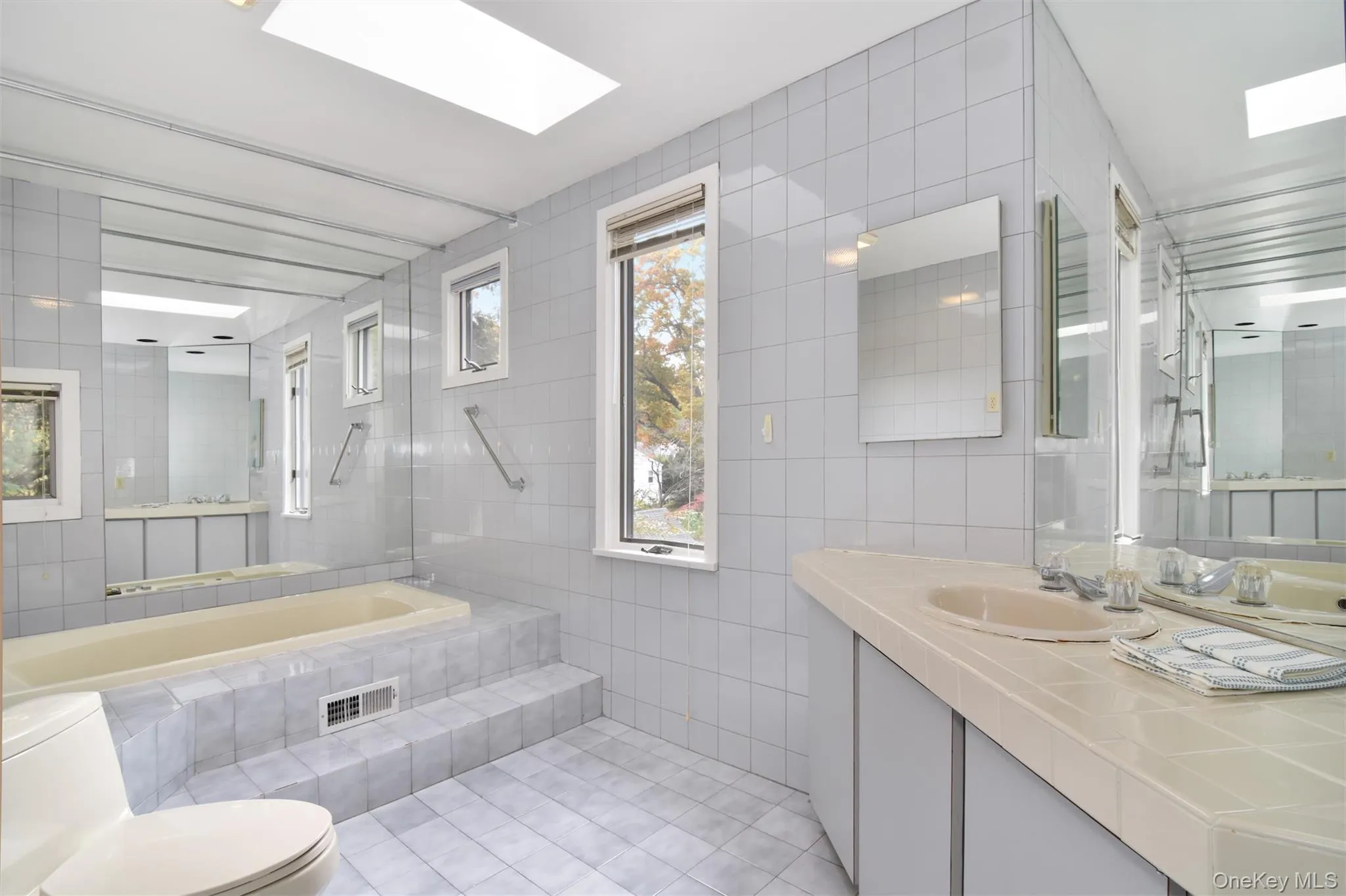 Primary Bathroom featuring tile walls, a skylight, light tile patterned floors, and vanity Primary Bathroom featuring tile walls, a skylight, light tile patterned floors, and vanity
