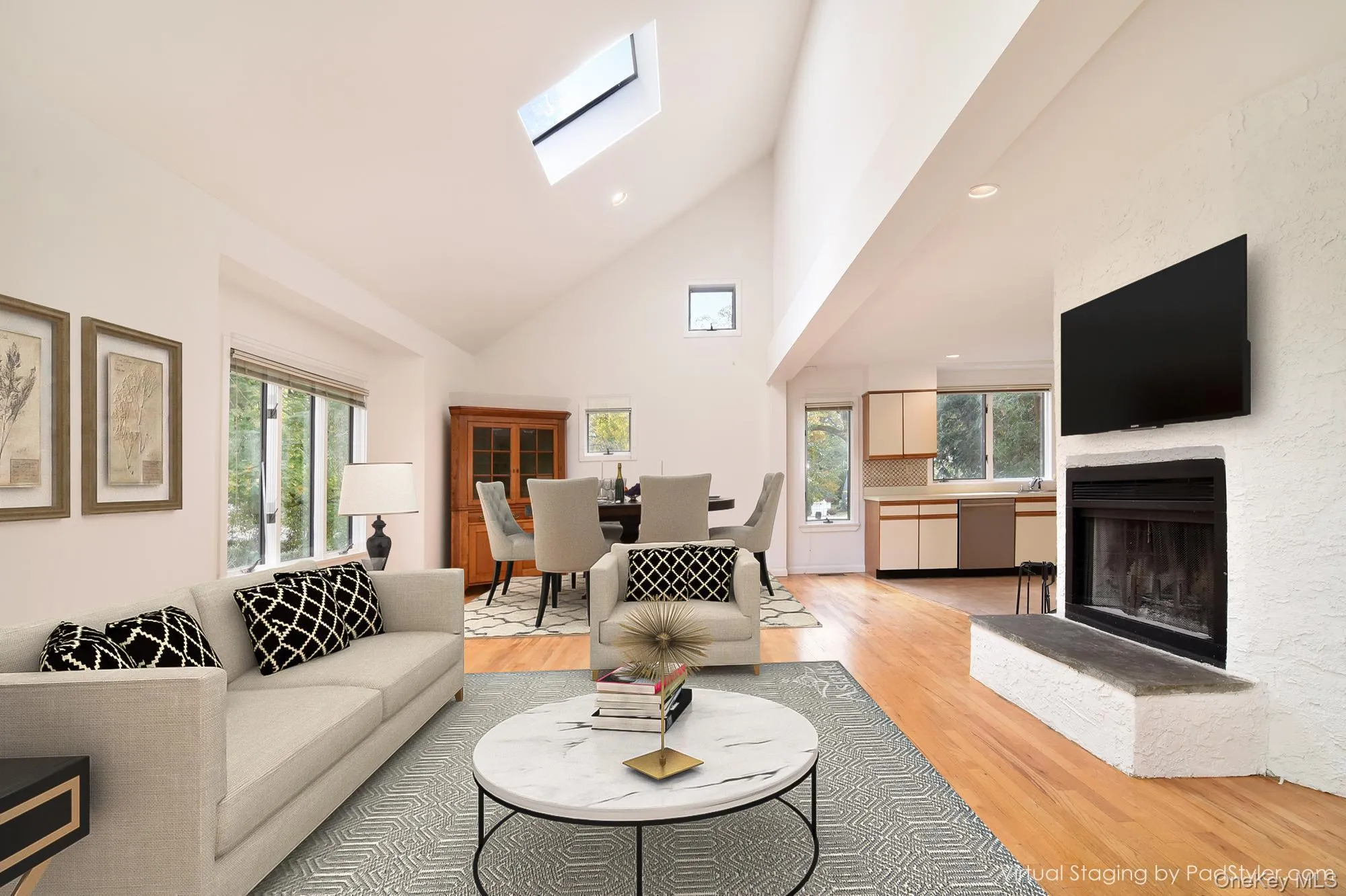 Virtually stagedLiving area with high vaulted ceiling, a skylight, light wood flooring, recessed lighting, and a fireplace with raised hearth Virtually stagedLiving area with high vaulted ceiling, a skylight, light wood flooring, recessed lighting, and a fireplace with raised hearth
