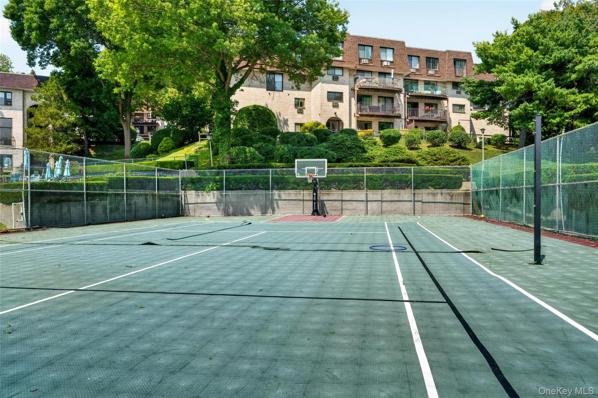 Multi-sport court featuring a basketball hoop and tennis net Multi-sport court featuring a basketball hoop and tennis net