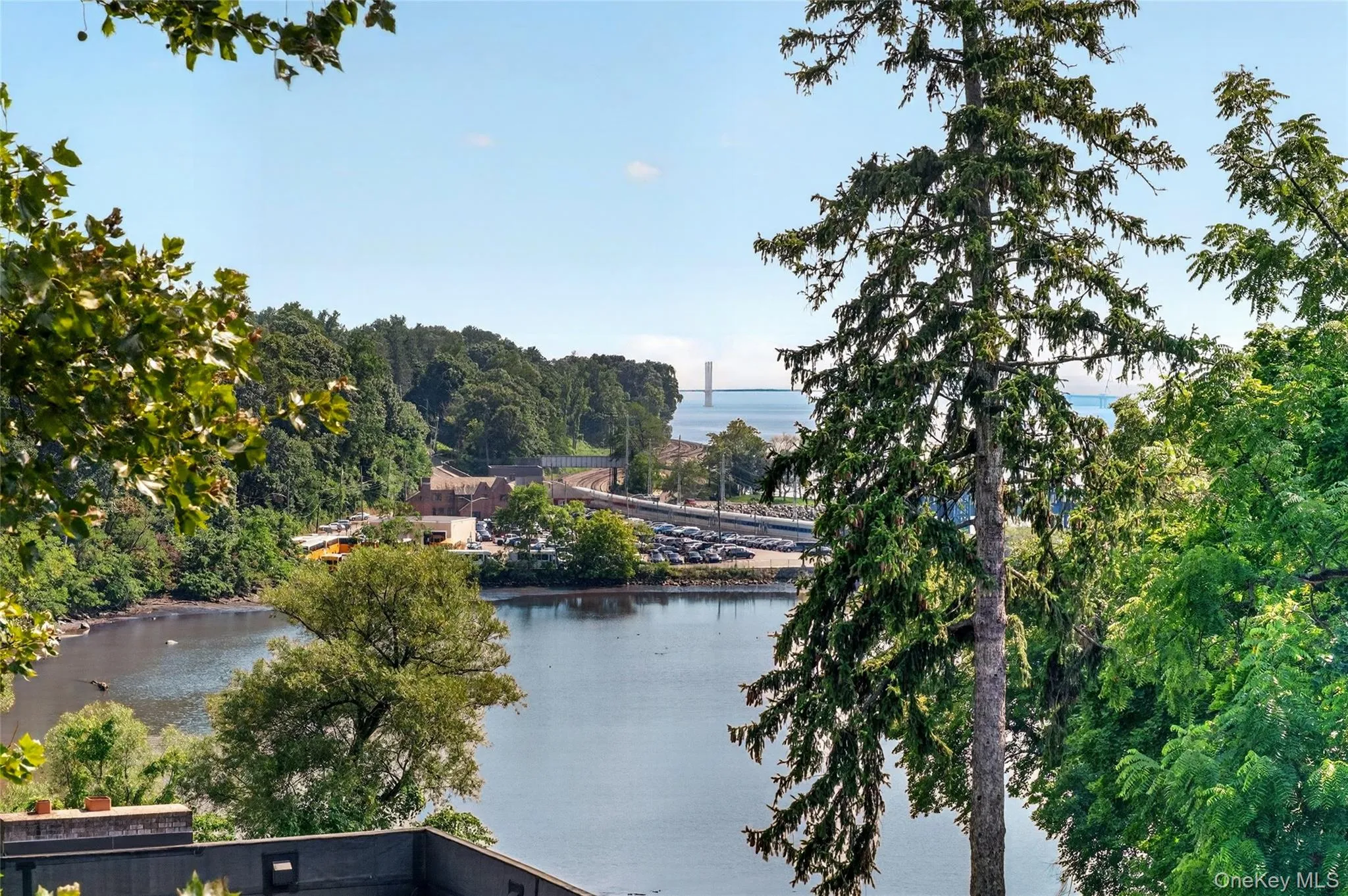 Expansive waterfront scenery from Primary Bedroom with mature trees framing a body of water and distant architectural structures Expansive waterfront scenery from Primary Bedroom with mature trees framing a body of water and distant architectural structures