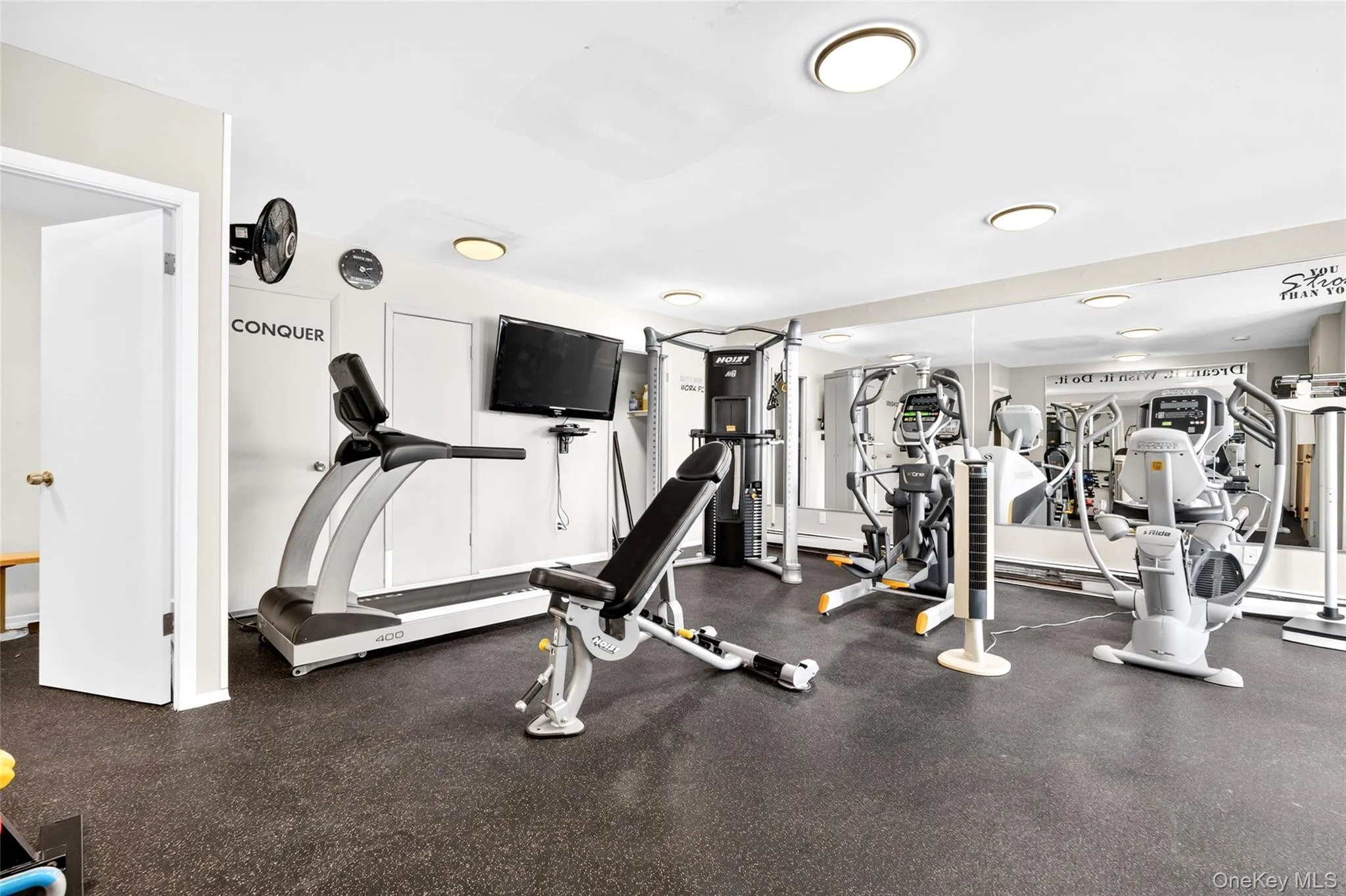 Dedicated fitness space featuring resilient rubber flooring, a wall-mounted television, and extensive mirror paneling Dedicated fitness space featuring resilient rubber flooring, a wall-mounted television, and extensive mirror paneling