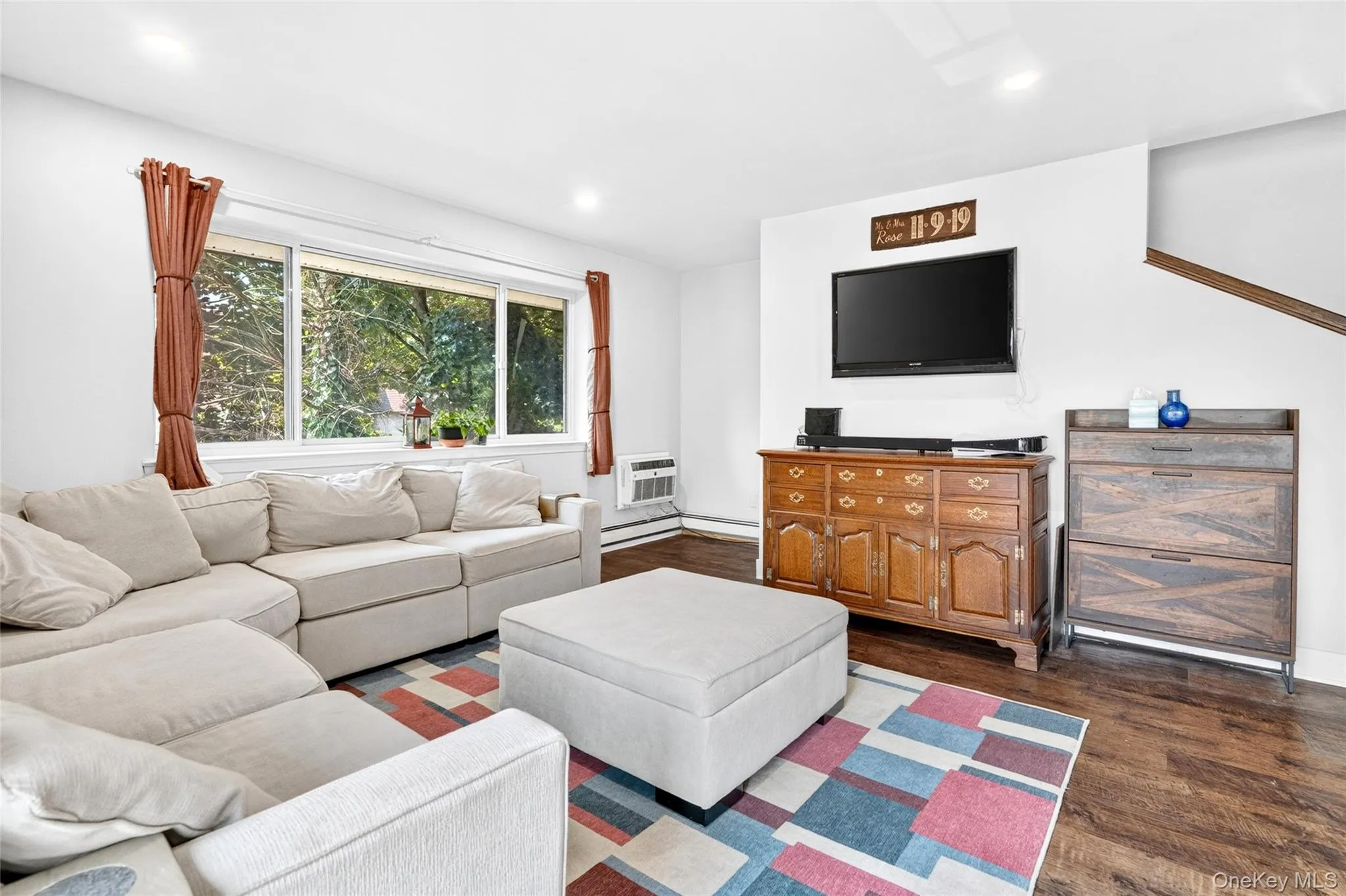 Living area featuring expansive window, recessed lighting, wood-finish flooring, and a staircase with wood railing Living area featuring expansive window, recessed lighting, wood-finish flooring, and a staircase with wood railing