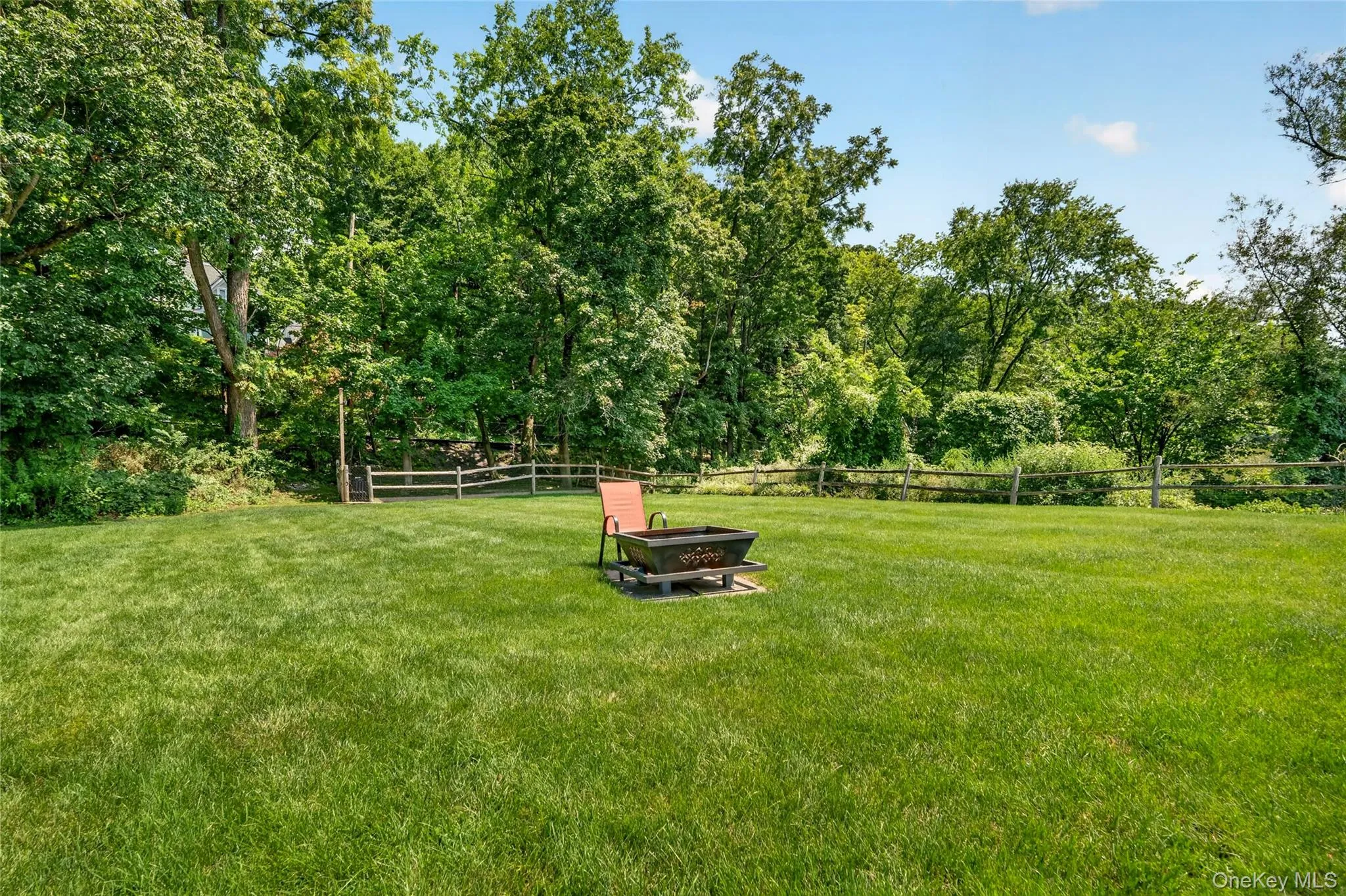 Expansive green lawn surrounded by mature trees and a rustic wood fence Expansive green lawn surrounded by mature trees and a rustic wood fence