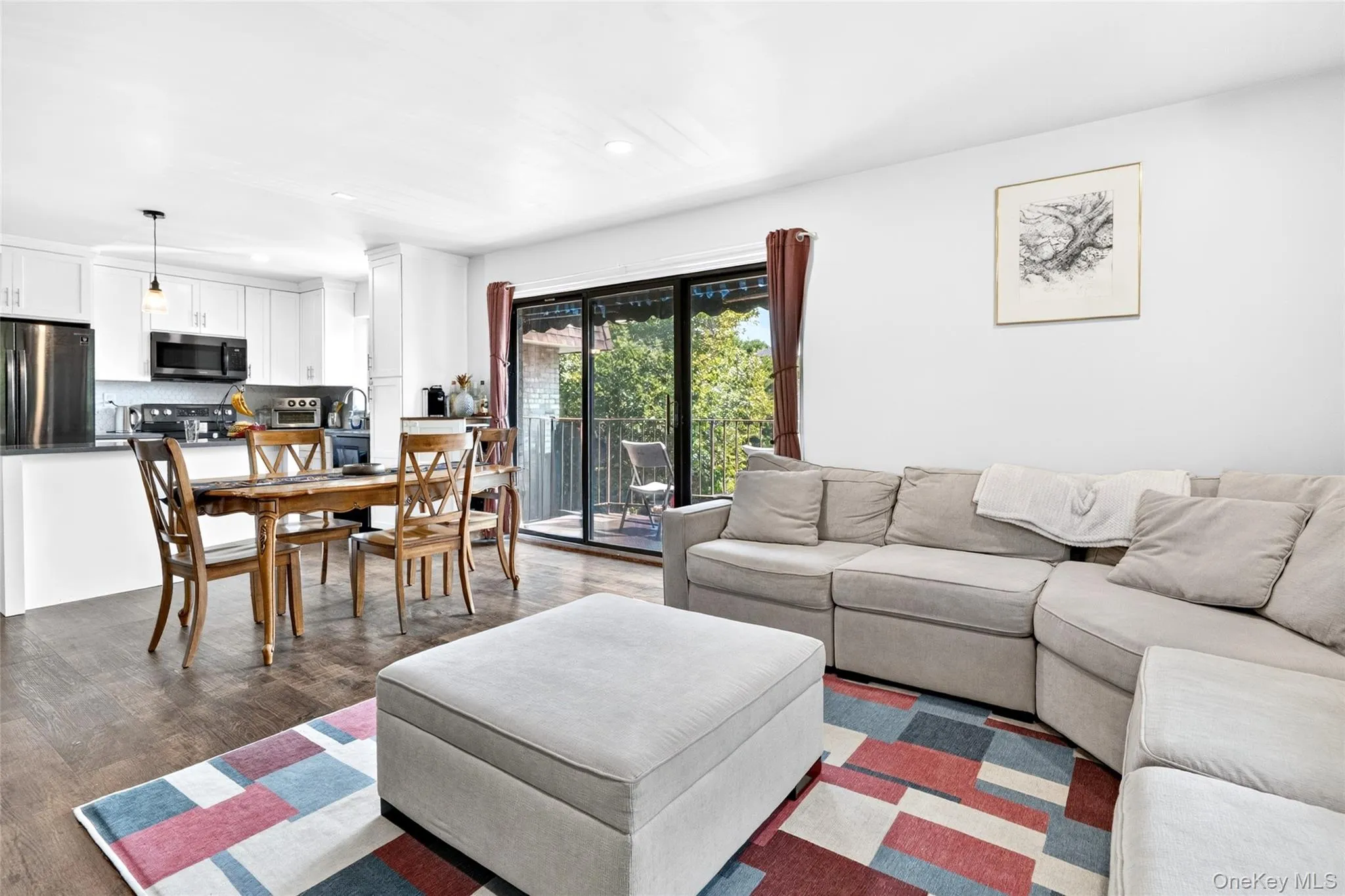 Open-concept living area featuring wood-finish flooring, a contemporary kitchen with stainless steel appliances, white cabinetry, and a peninsula Open-concept living area featuring wood-finish flooring, a contemporary kitchen with stainless steel appliances, white cabinetry, and a peninsula