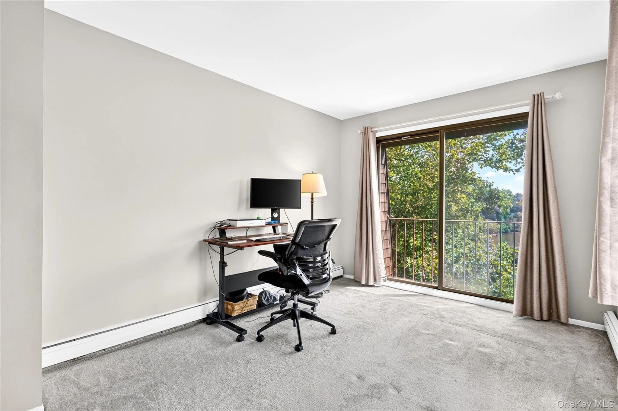 Sliding glass door leading to a balcony with metal railing, soft gray carpeting, light-colored wall paint, and white baseboards Sliding glass door leading to a balcony with metal railing, soft gray carpeting, light-colored wall paint, and white baseboards