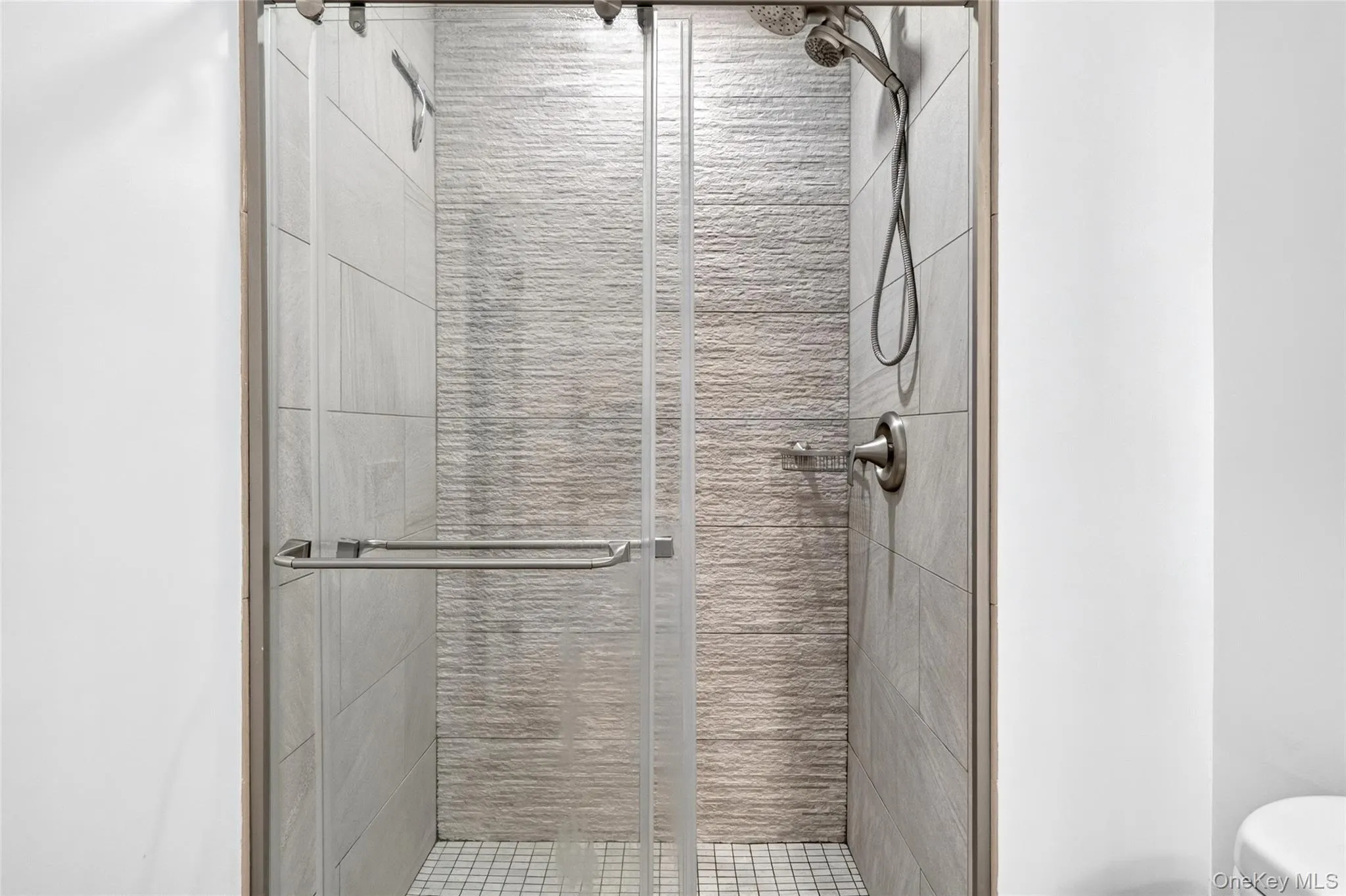 Glass-enclosed shower with brushed nickel fixtures, a rain showerhead, a handheld shower, and a textured tile accent wall Glass-enclosed shower with brushed nickel fixtures, a rain showerhead, a handheld shower, and a textured tile accent wall