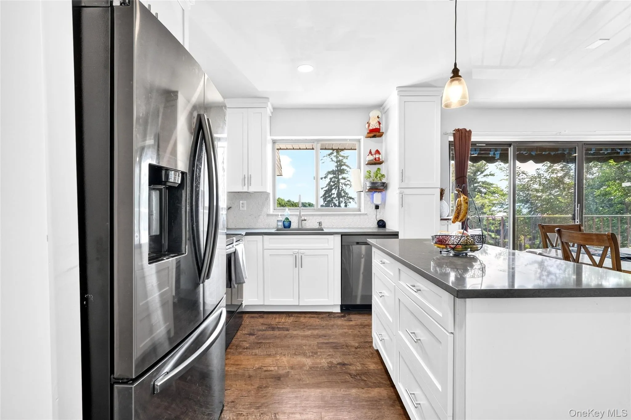 Kitchen featuring wood-finish flooring, white cabinetry, dark countertops, and stainless steel appliances Kitchen featuring wood-finish flooring, white cabinetry, dark countertops, and stainless steel appliances
