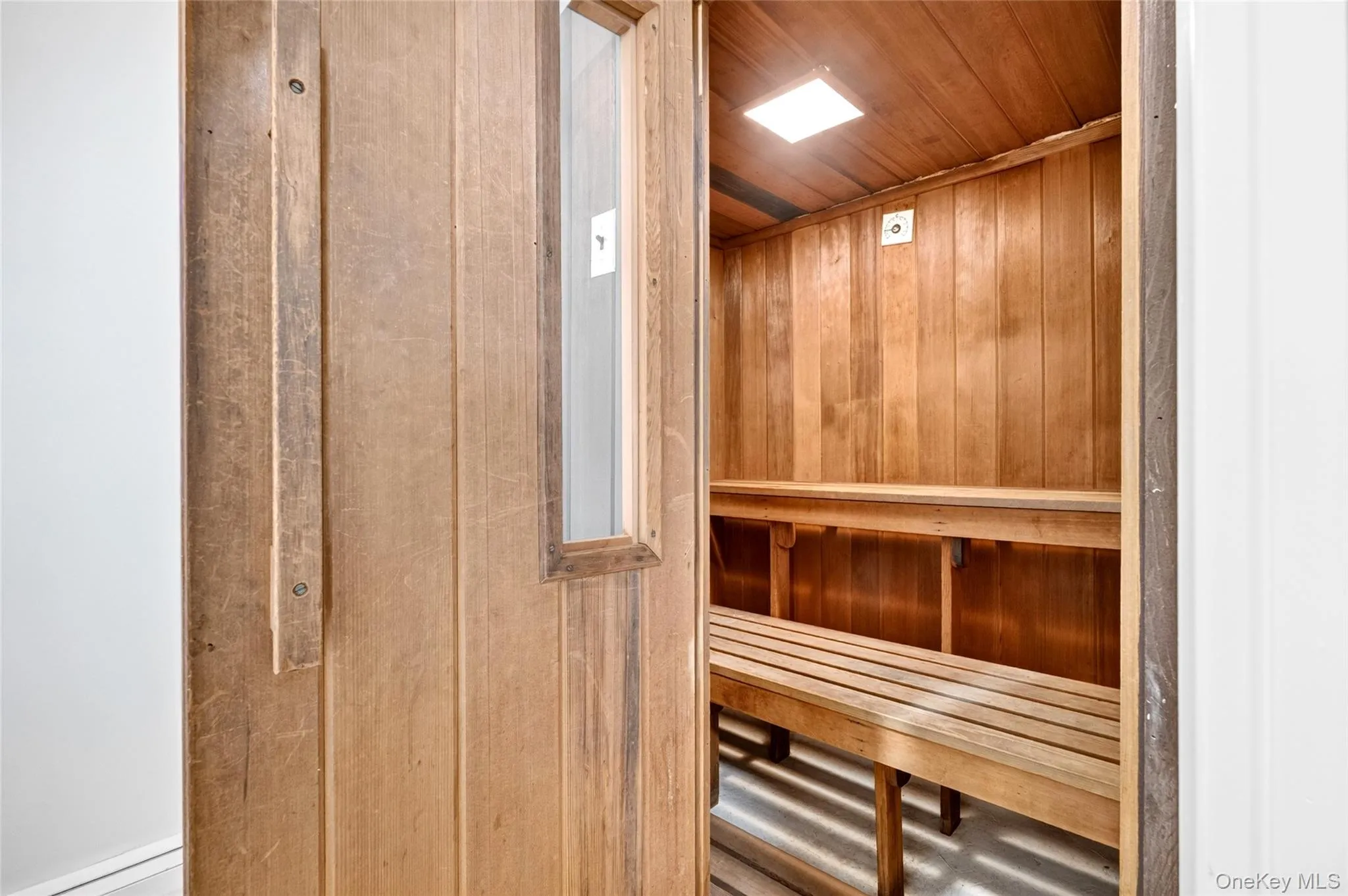 Built-in sauna featuring light wood paneling, multiple tiered benches, a small interior window, and recessed ceiling lighting Built-in sauna featuring light wood paneling, multiple tiered benches, a small interior window, and recessed ceiling lighting