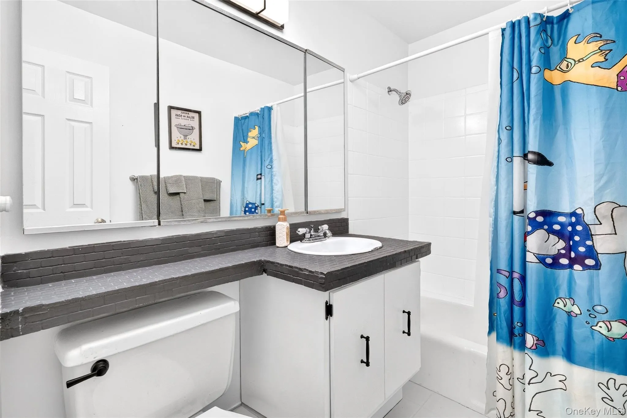 Bathroom featuring a white vanity with an integrated sink, dark countertop, and a medicine cabinet with mirror panels Bathroom featuring a white vanity with an integrated sink, dark countertop, and a medicine cabinet with mirror panels