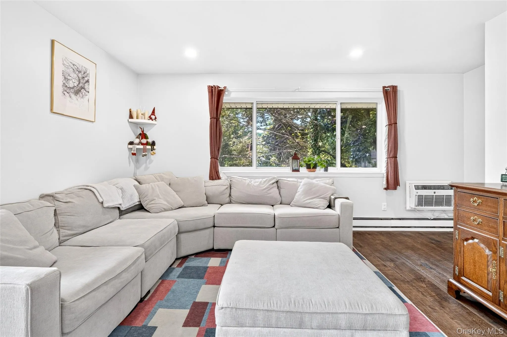 Bright living area featuring wood-finish flooring, a large window, white walls, recessed lighting, and baseboard heating Bright living area featuring wood-finish flooring, a large window, white walls, recessed lighting, and baseboard heating