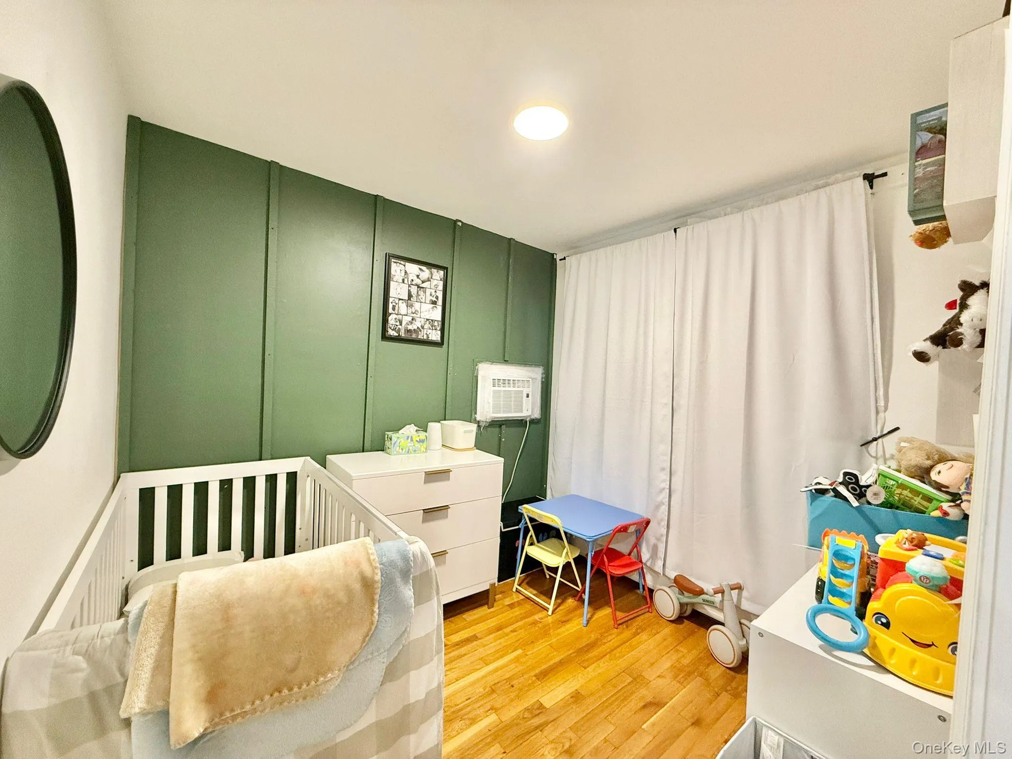 Room featuring a green accent wall with vertical paneling, light wood-finish flooring, and a white ceiling Room featuring a green accent wall with vertical paneling, light wood-finish flooring, and a white ceiling