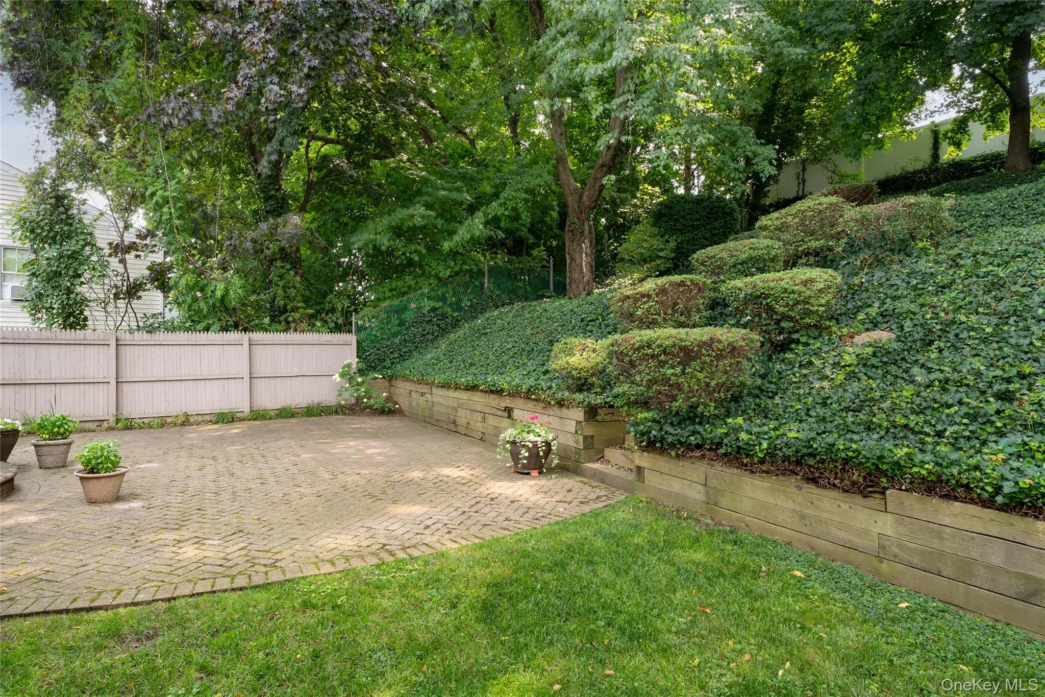 Expansive outdoor space featuring a paver patio and a tiered retaining wall Expansive outdoor space featuring a paver patio and a tiered retaining wall