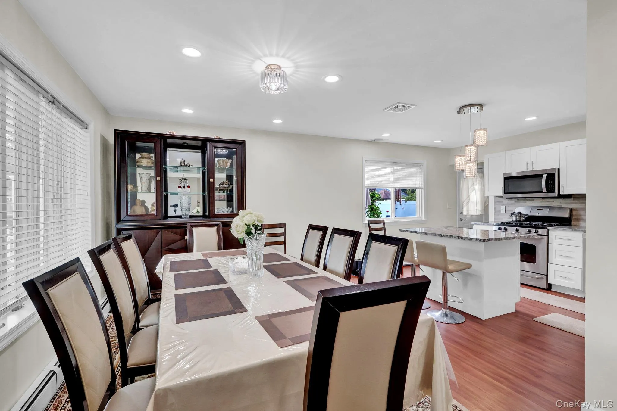 Bright dining area with wood-finish flooring, recessed lighting, and a crystal chandelier Bright dining area with wood-finish flooring, recessed lighting, and a crystal chandelier