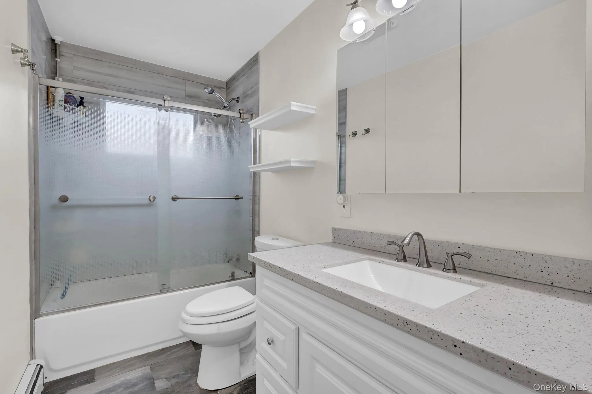 Bathroom featuring a white vanity with paneling, a light-toned speckled countertop, an undermount sink with a brushed nickel faucet, and a mirrored medicine cabinet Bathroom featuring a white vanity with paneling, a light-toned speckled countertop, an undermount sink with a brushed nickel faucet, and a mirrored medicine cabinet