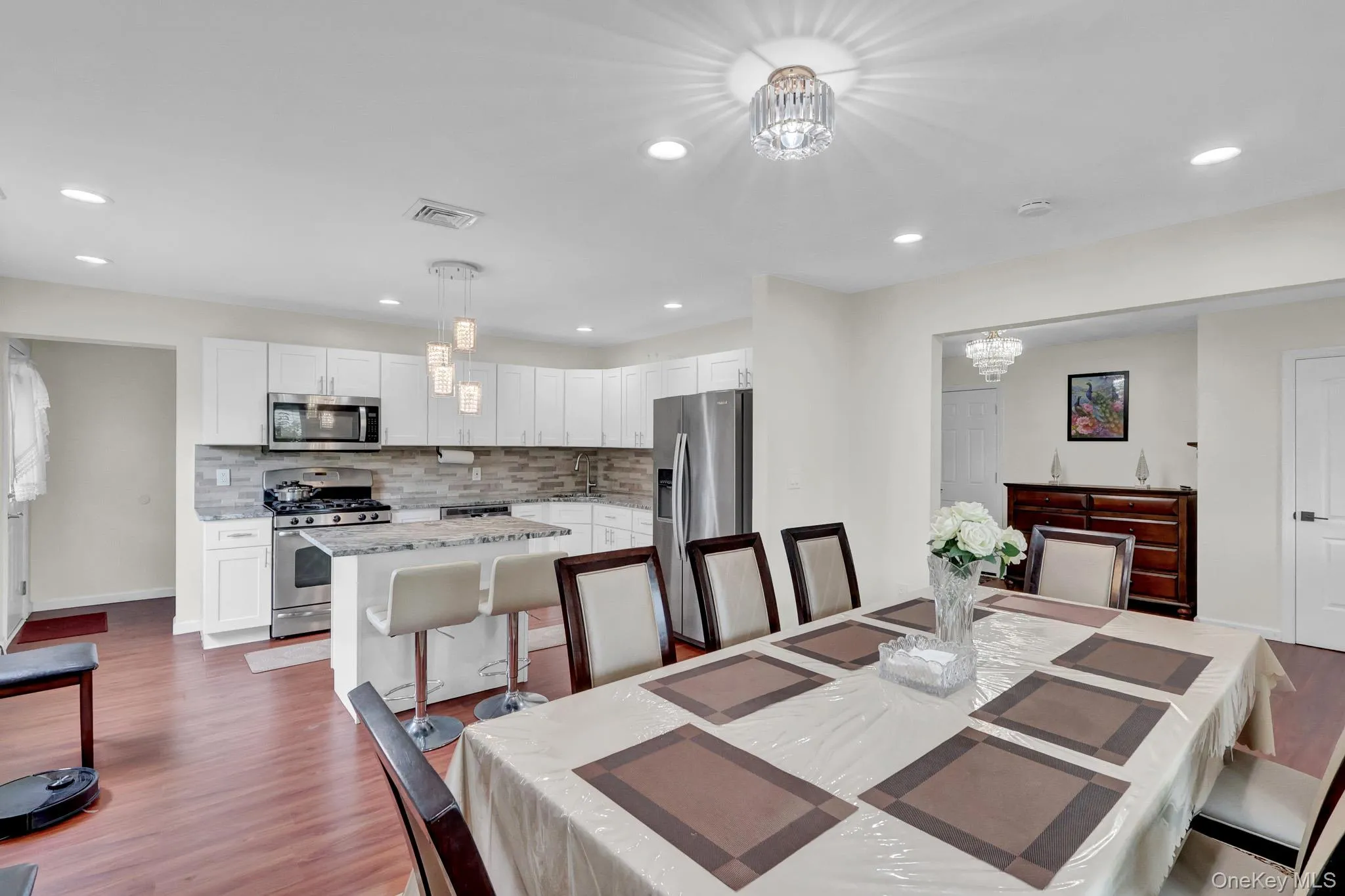 Modern kitchen featuring white cabinetry, stainless steel appliances, a stone-finish backsplash, and an island with counter seating Modern kitchen featuring white cabinetry, stainless steel appliances, a stone-finish backsplash, and an island with counter seating