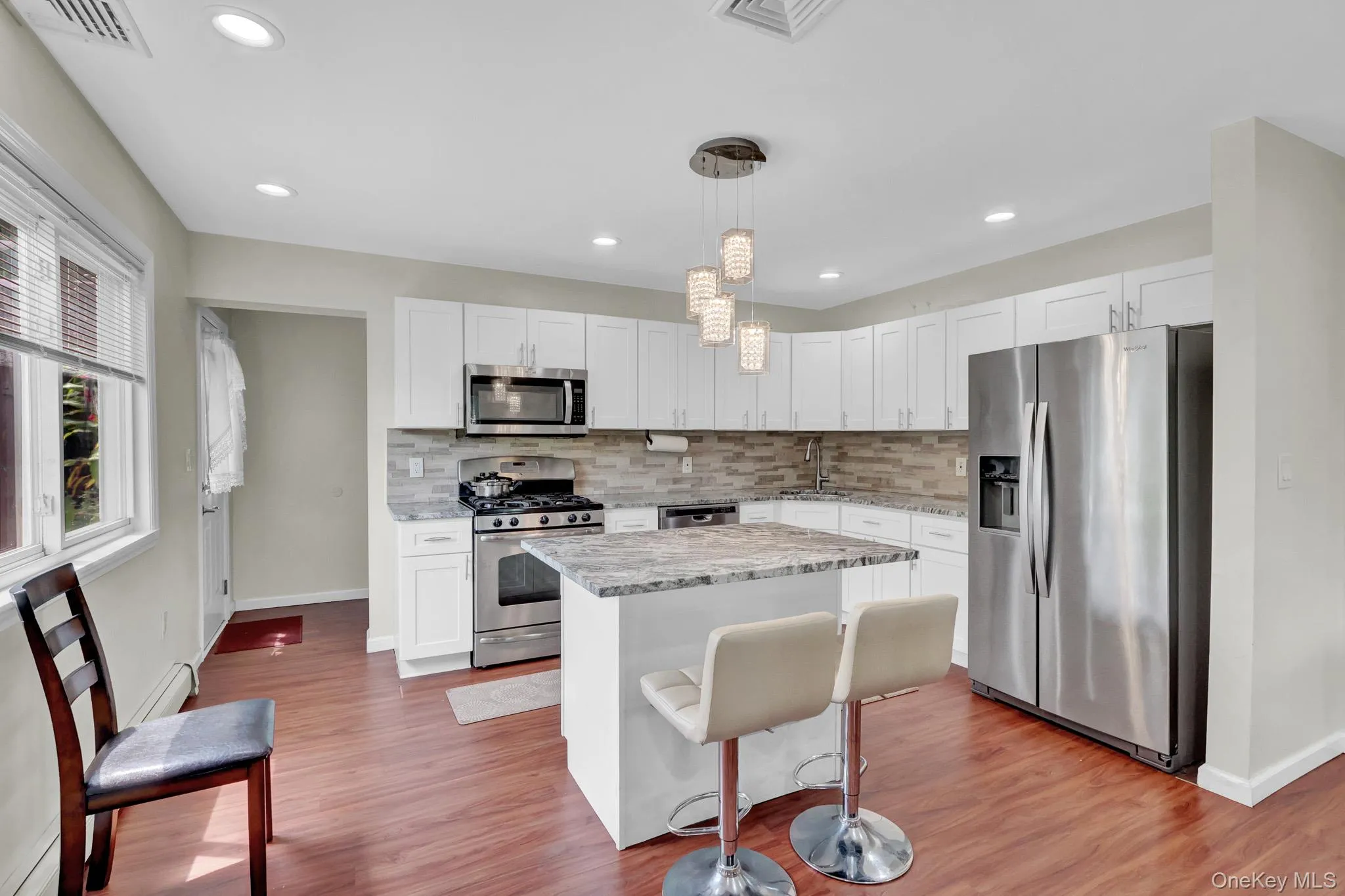 Modern kitchen featuring white cabinetry, stainless steel appliances, a center island with countertop seating, wood-finish flooring, and recessed lighting Modern kitchen featuring white cabinetry, stainless steel appliances, a center island with countertop seating, wood-finish flooring, and recessed lighting