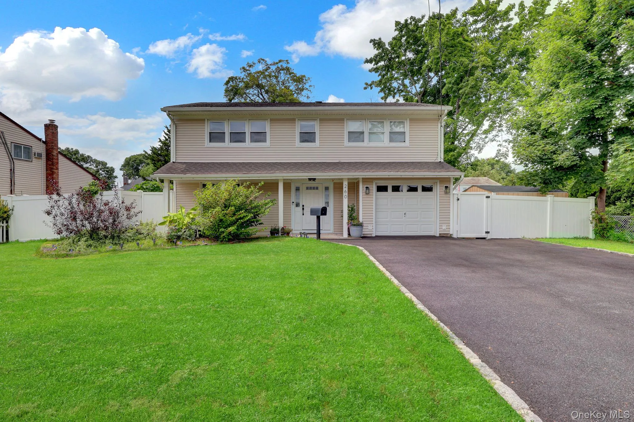 Two-story residence featuring light-colored siding, a covered front entry, and an attached garage with a white door Two-story residence featuring light-colored siding, a covered front entry, and an attached garage with a white door