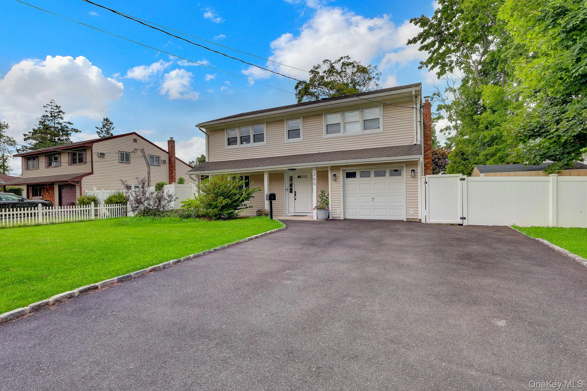 Two-story residence featuring light-colored siding, an attached garage, a paved driveway, and a white privacy fence Two-story residence featuring light-colored siding, an attached garage, a paved driveway, and a white privacy fence