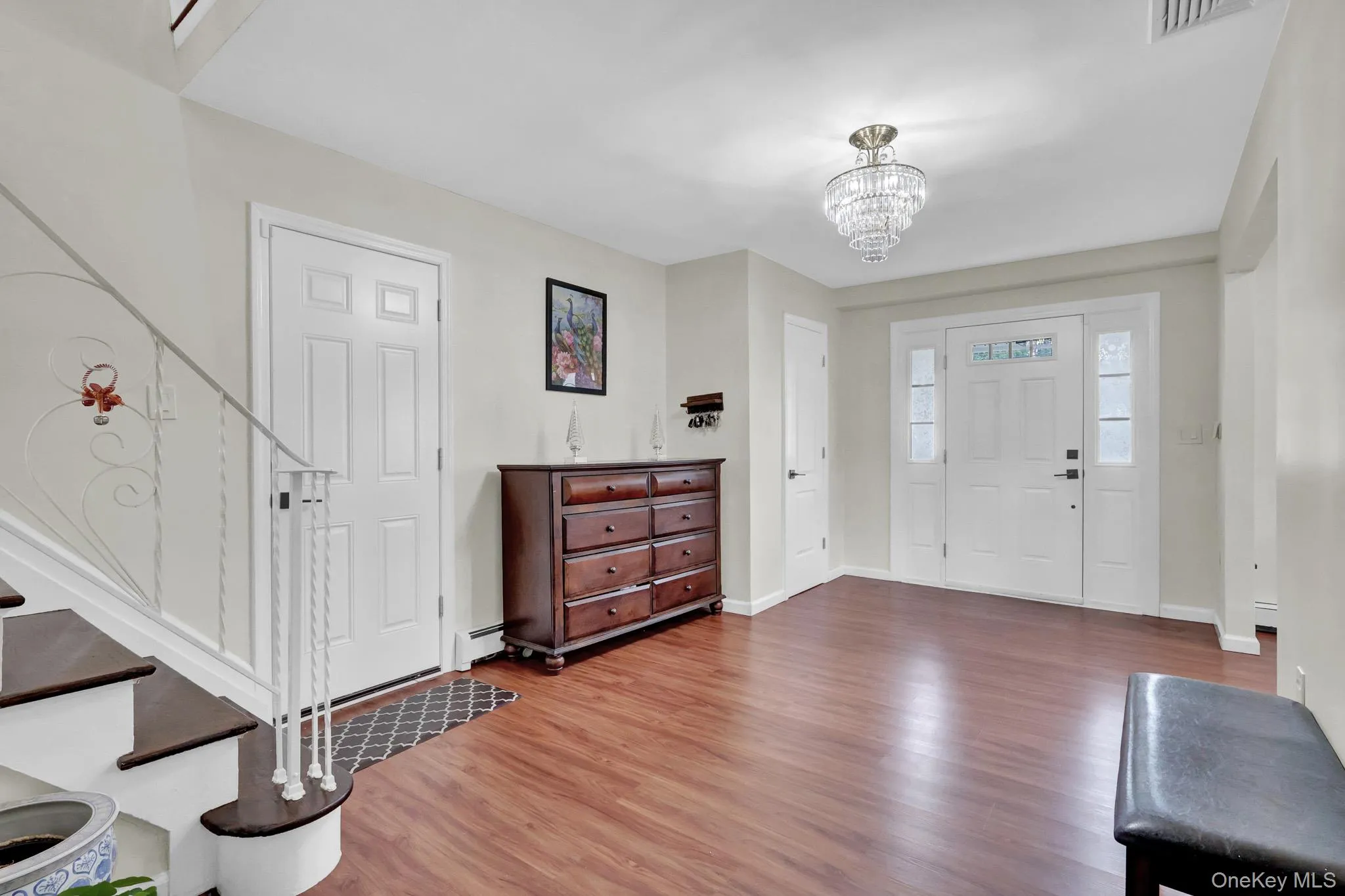 Entryway featuring wood-finish flooring, a white front door with sidelight windows, and a multi-tiered crystal chandelier Entryway featuring wood-finish flooring, a white front door with sidelight windows, and a multi-tiered crystal chandelier