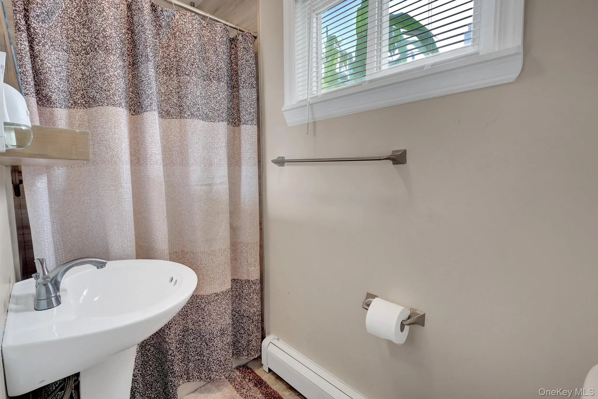 Bathroom featuring a pedestal sink with a chrome faucet, a window with blinds, and a built-in radiator Bathroom featuring a pedestal sink with a chrome faucet, a window with blinds, and a built-in radiator