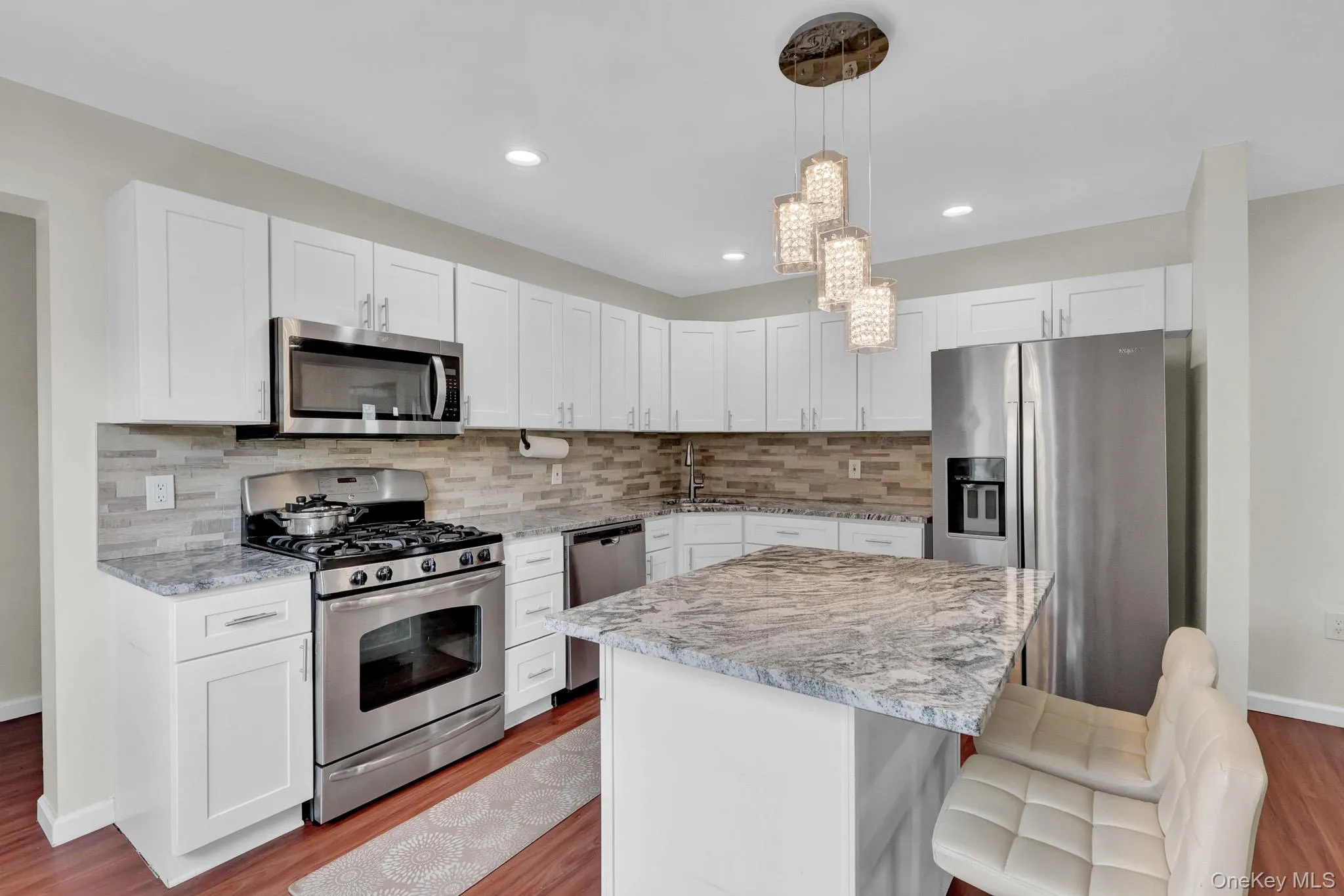 Kitchen featuring white shaker cabinetry, stainless steel appliances, a multi-tone tile backsplash, and a central island with a stone countertop Kitchen featuring white shaker cabinetry, stainless steel appliances, a multi-tone tile backsplash, and a central island with a stone countertop