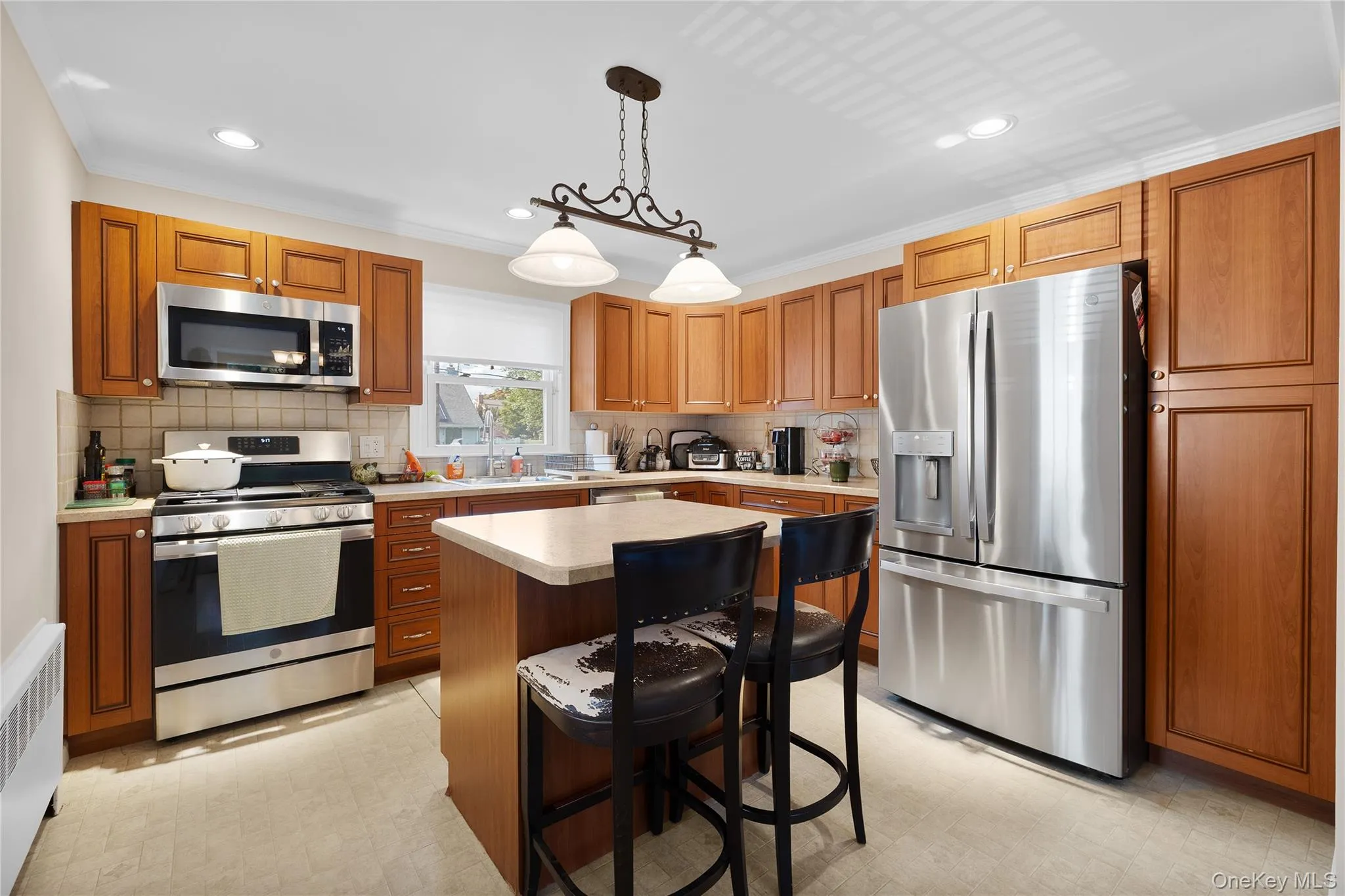 Kitchen featuring wood cabinetry, stainless steel appliances, a center island with countertop seating, recessed lighting, and a window above the sink Kitchen featuring wood cabinetry, stainless steel appliances, a center island with countertop seating, recessed lighting, and a window above the sink