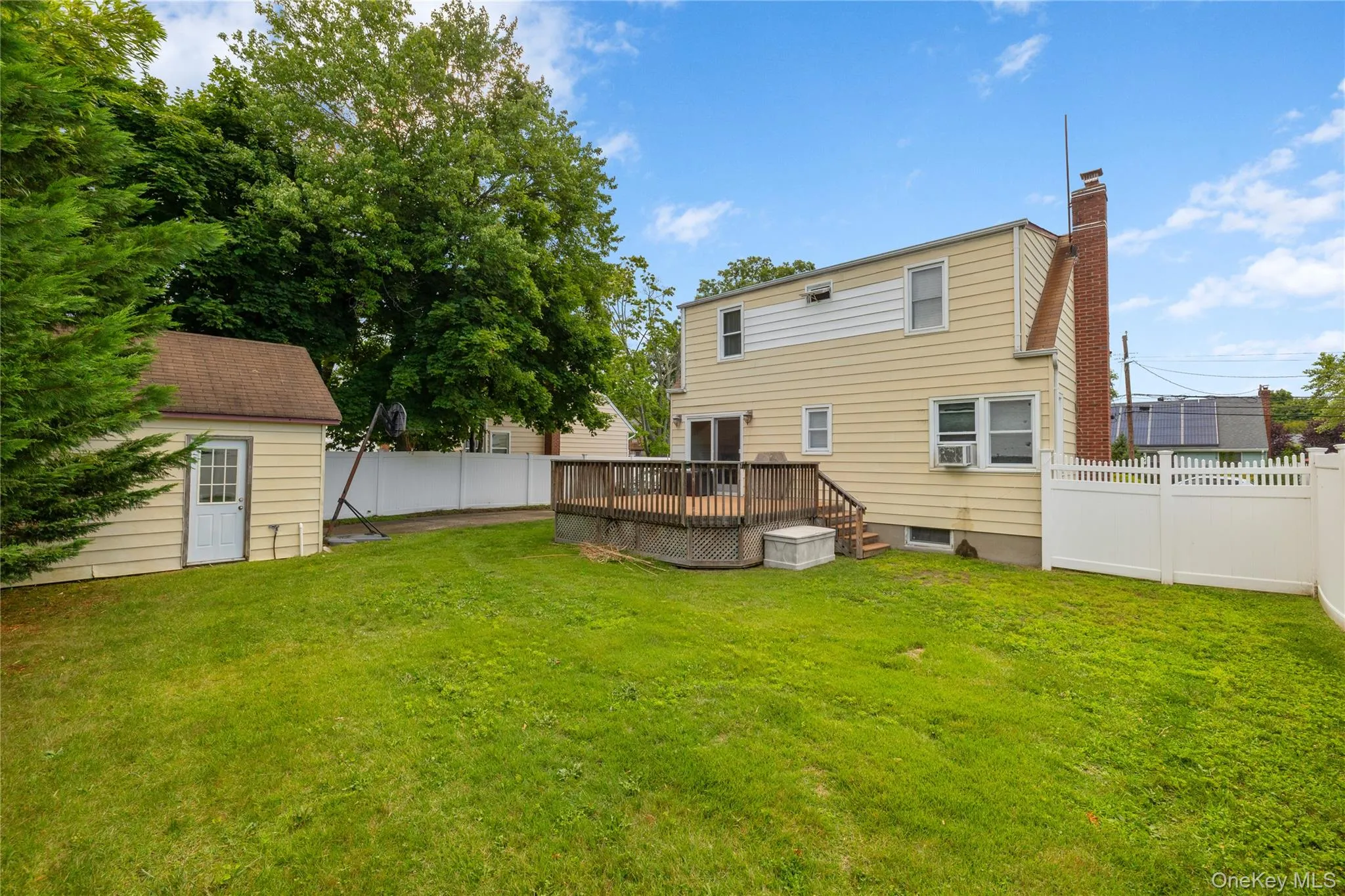 Expansive rear yard featuring a wooden deck, a detached storage shed, and a white picket fence enclosing the perimeter Expansive rear yard featuring a wooden deck, a detached storage shed, and a white picket fence enclosing the perimeter