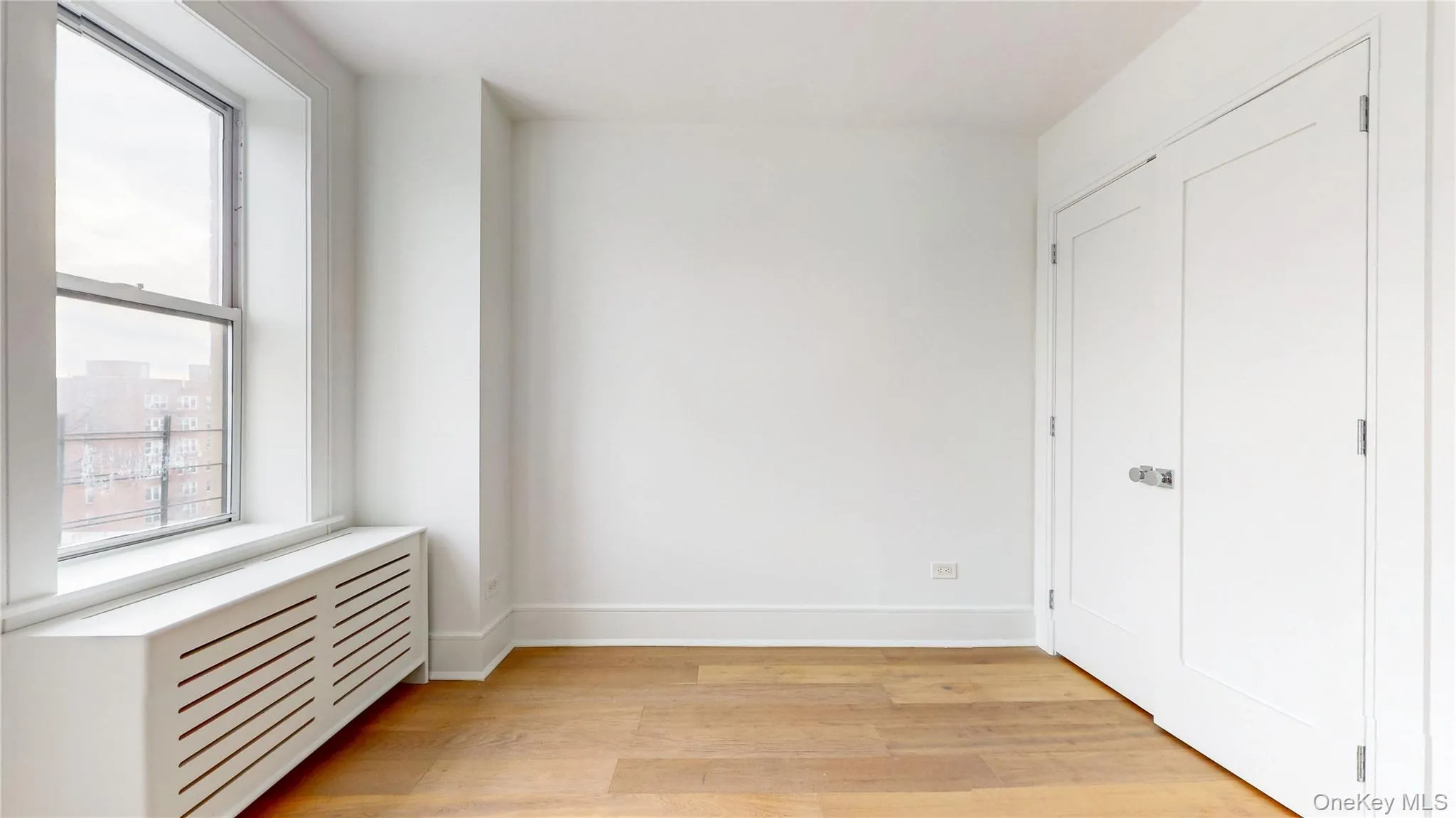 Bright room featuring wood-finish flooring, crisp white walls, and a large window with a white radiator cover Bright room featuring wood-finish flooring, crisp white walls, and a large window with a white radiator cover