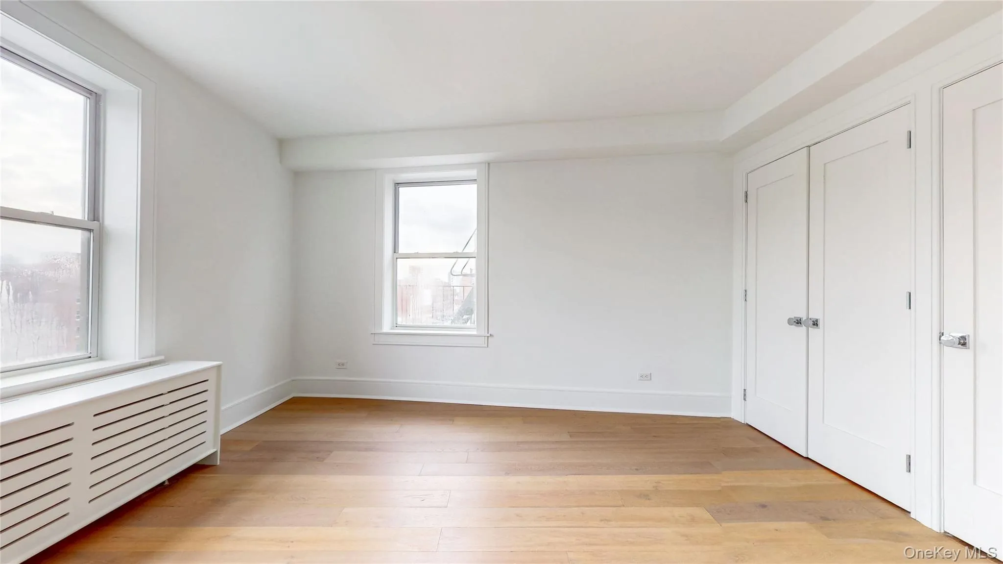 Bright interior space featuring wood-finish flooring, white walls, two sash windows, and two white panel doors with contemporary hardware Bright interior space featuring wood-finish flooring, white walls, two sash windows, and two white panel doors with contemporary hardware