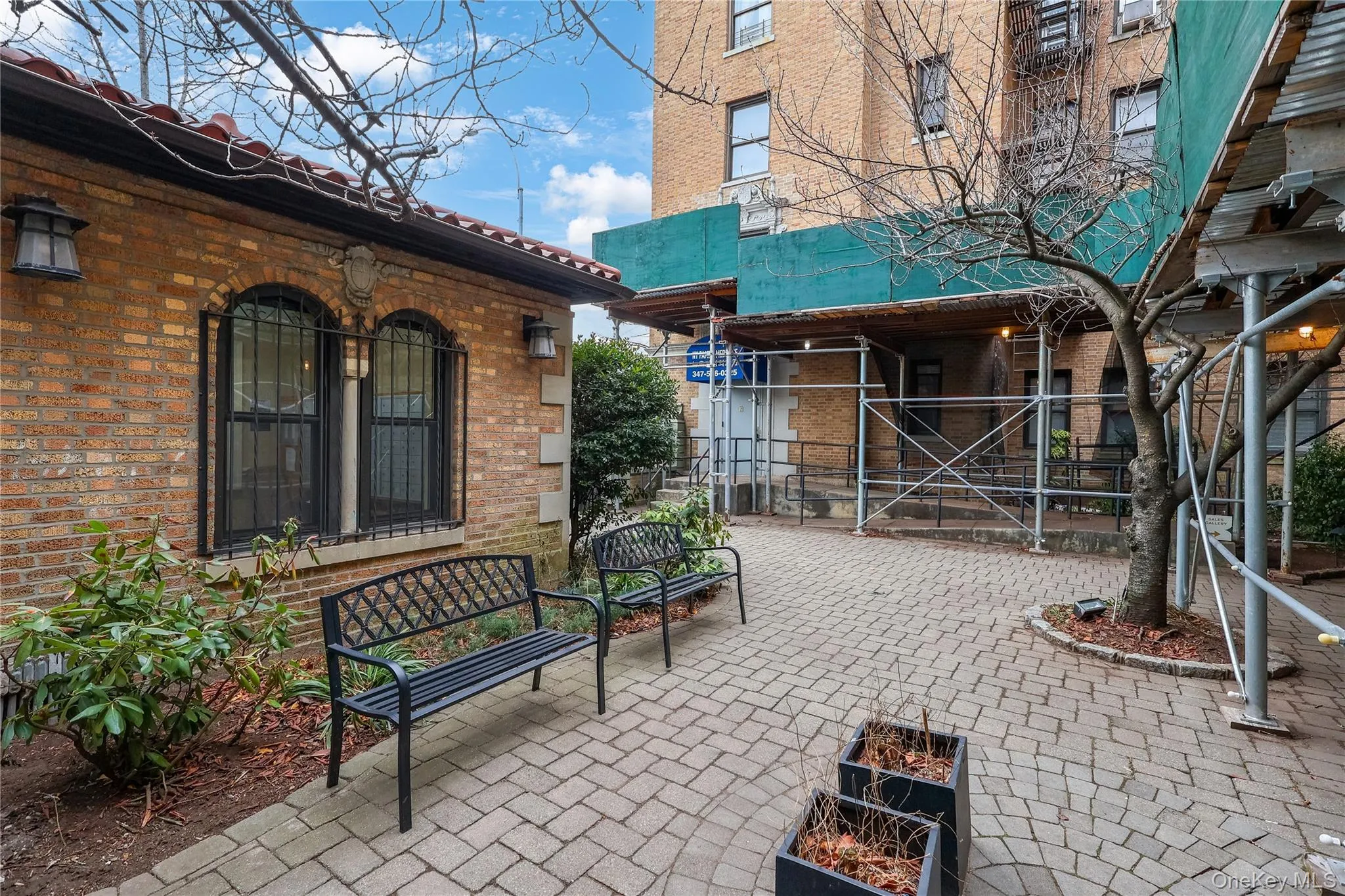 Paved patio area featuring a brick exterior with arched windows, exterior wall sconces, and a terra cotta tile roof Paved patio area featuring a brick exterior with arched windows, exterior wall sconces, and a terra cotta tile roof